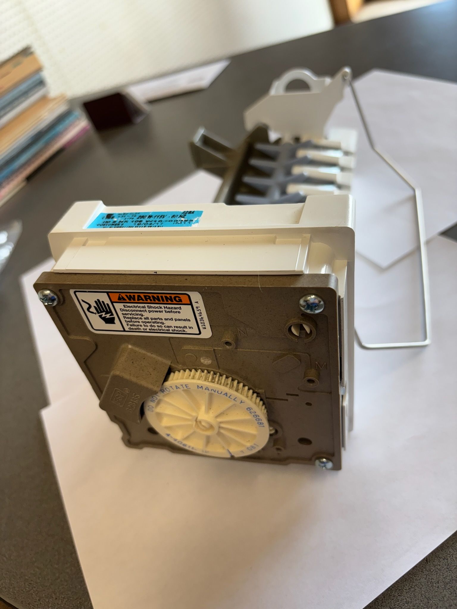Ice maker assembly with a white gear, on a surface with paper.
