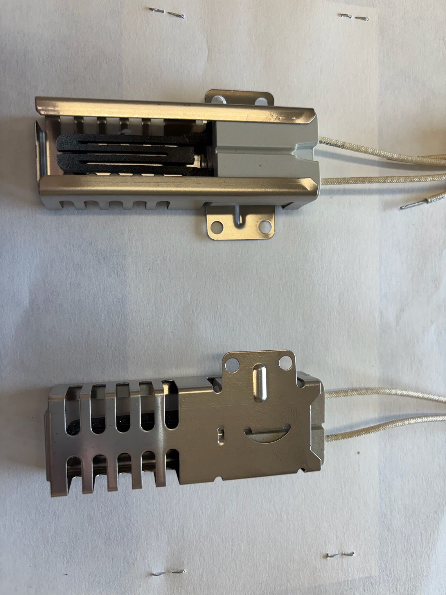 Two silver oven igniters with wire leads, set against a white surface.