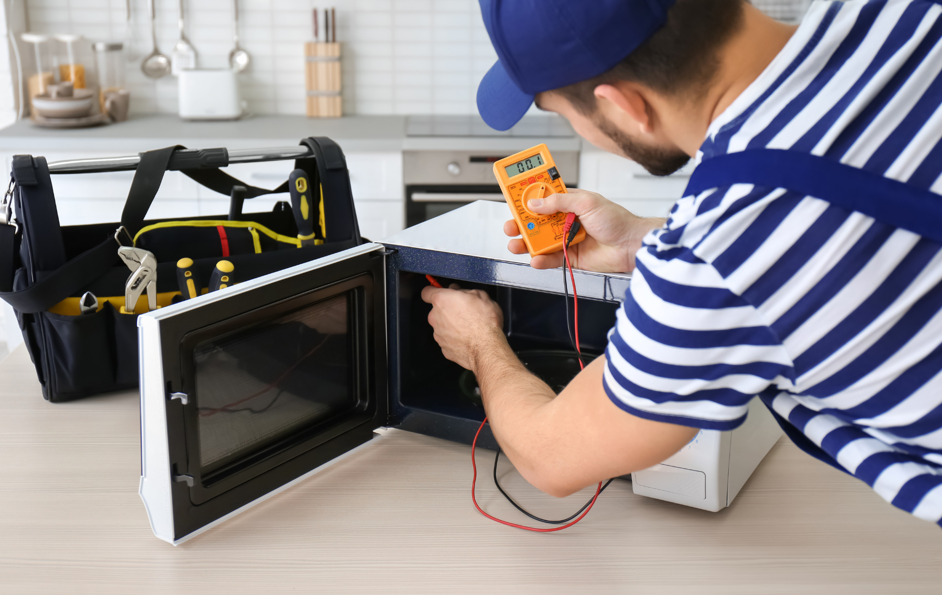 A man is fixing a microwave with a multimeter.