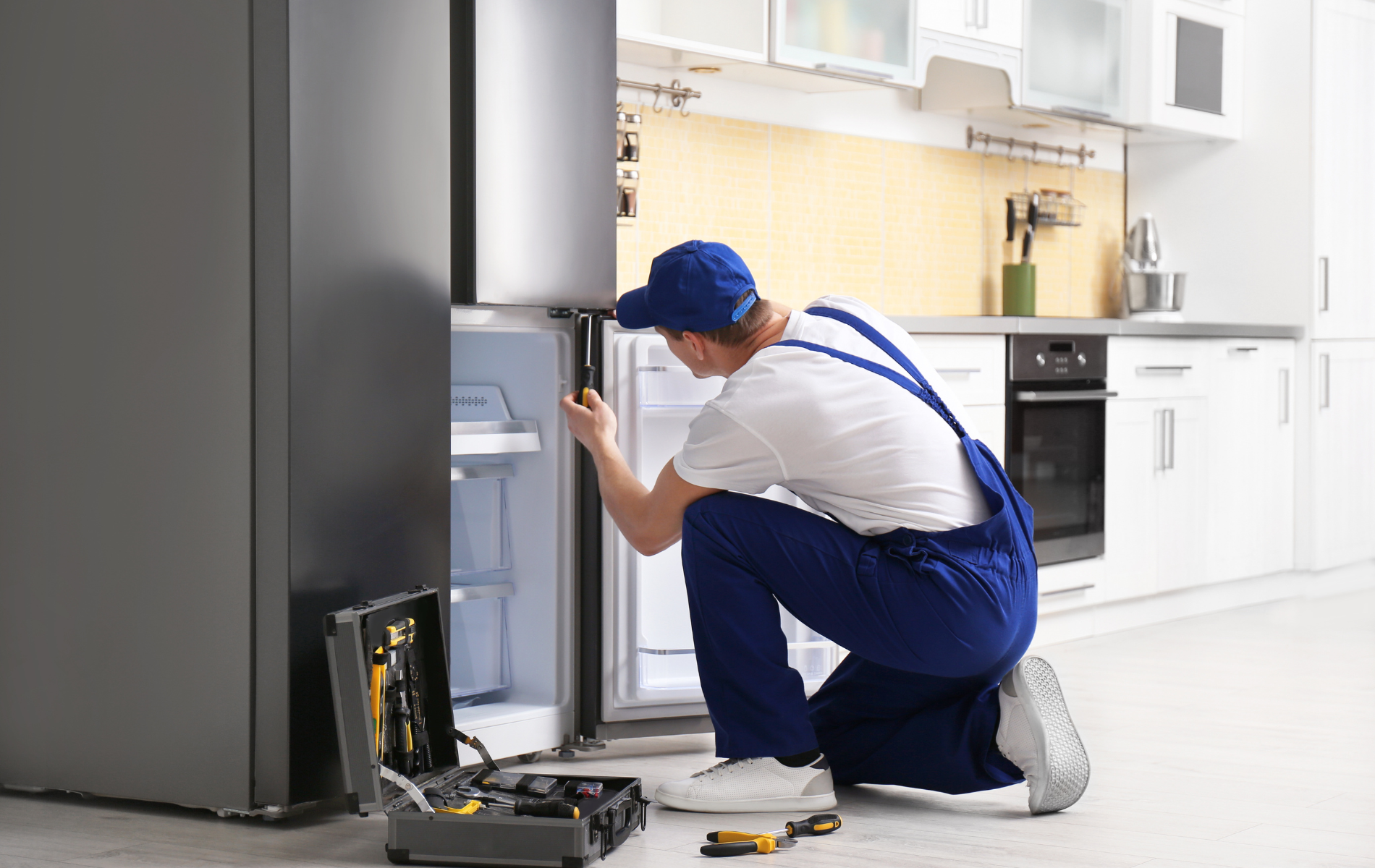 A man is repairing a refrigerator in a kitchen.