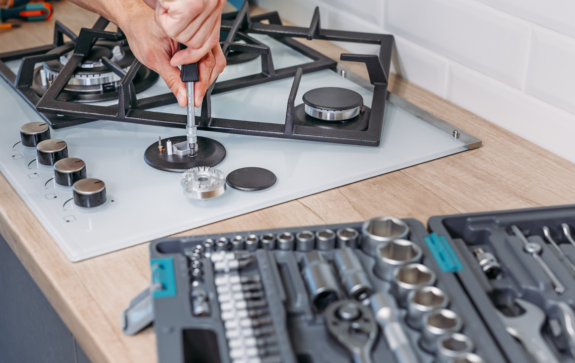 A person is fixing a gas stove with a screwdriver.