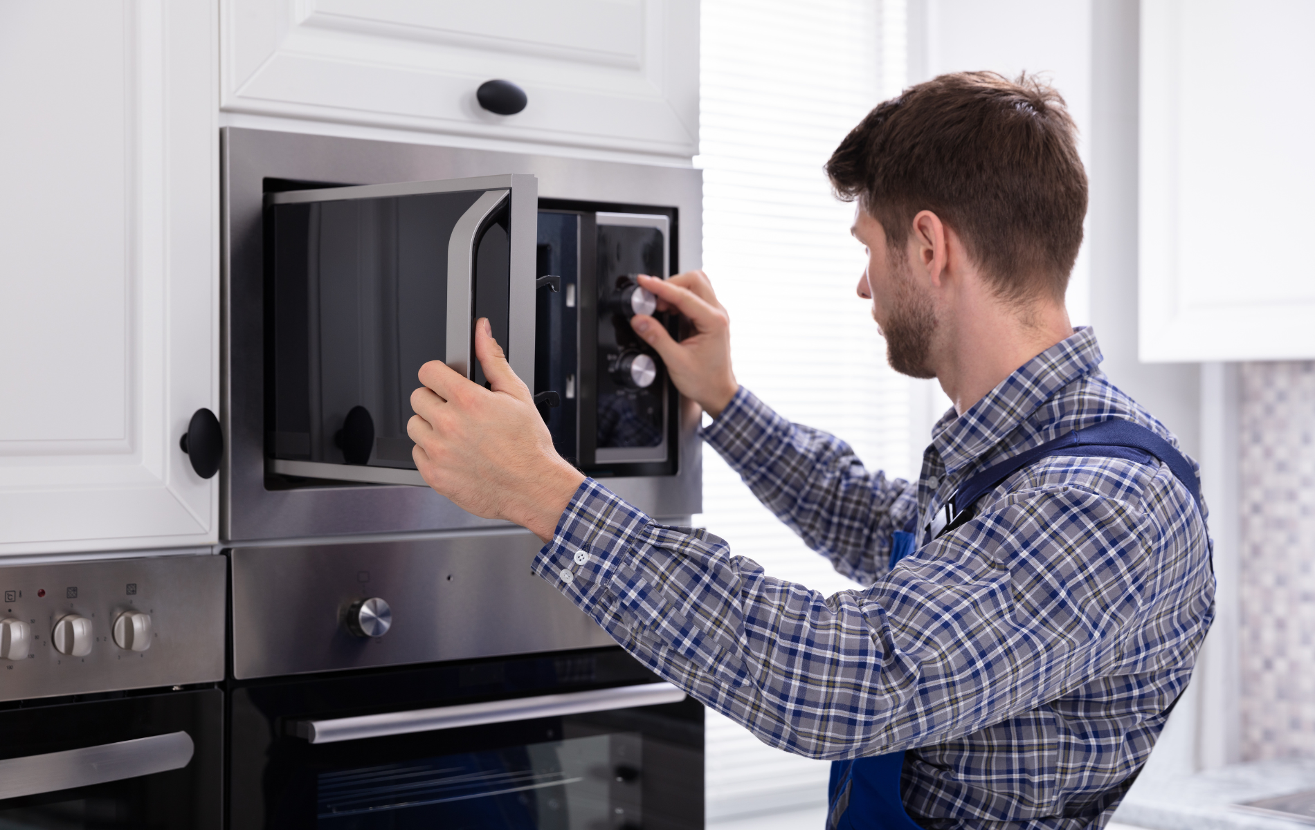 A man is fixing a microwave oven in a kitchen.