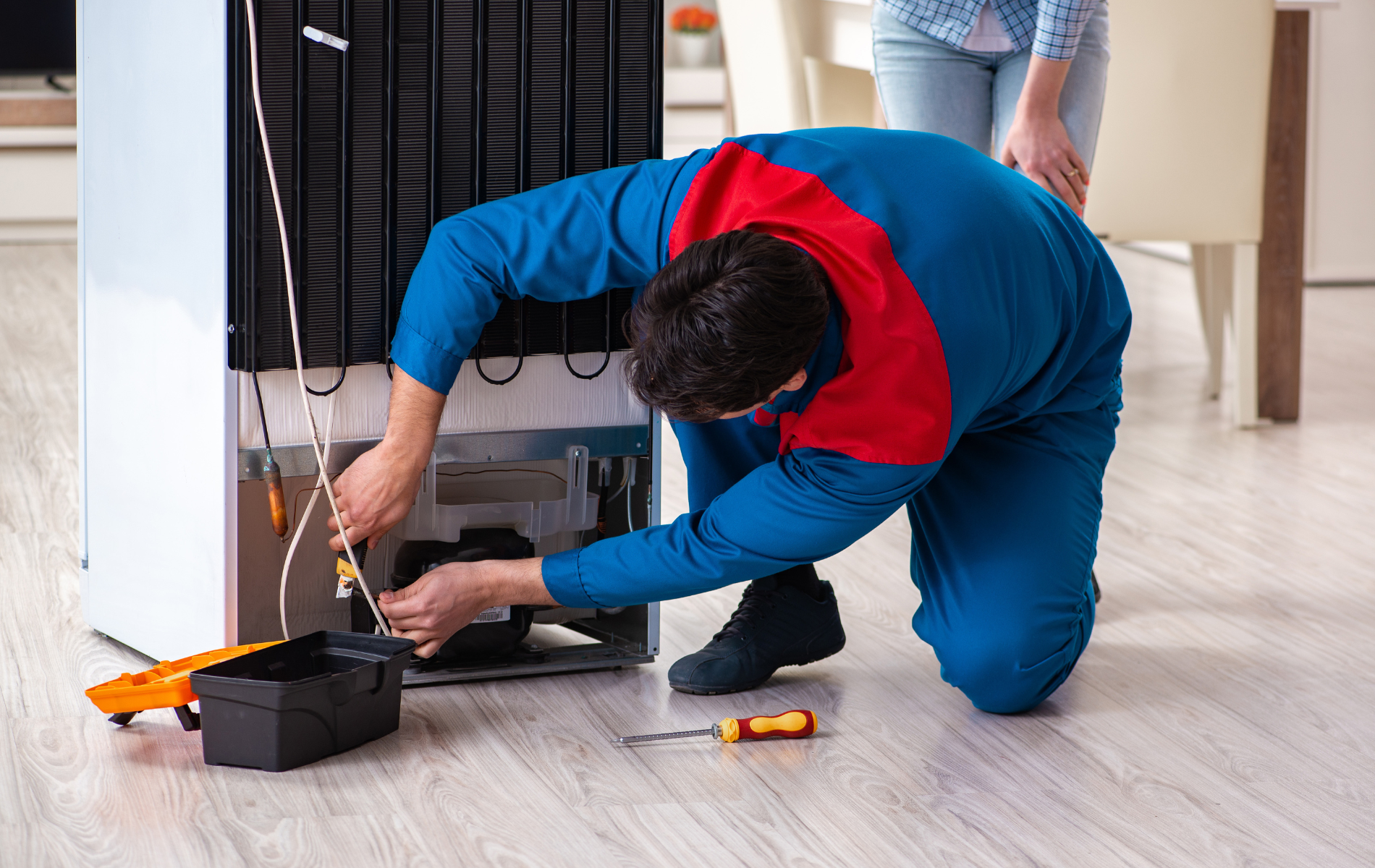 A man is fixing a refrigerator in a kitchen.