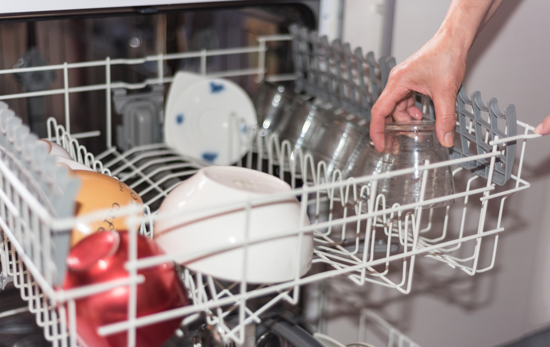 A person is putting a glass in a dishwasher.