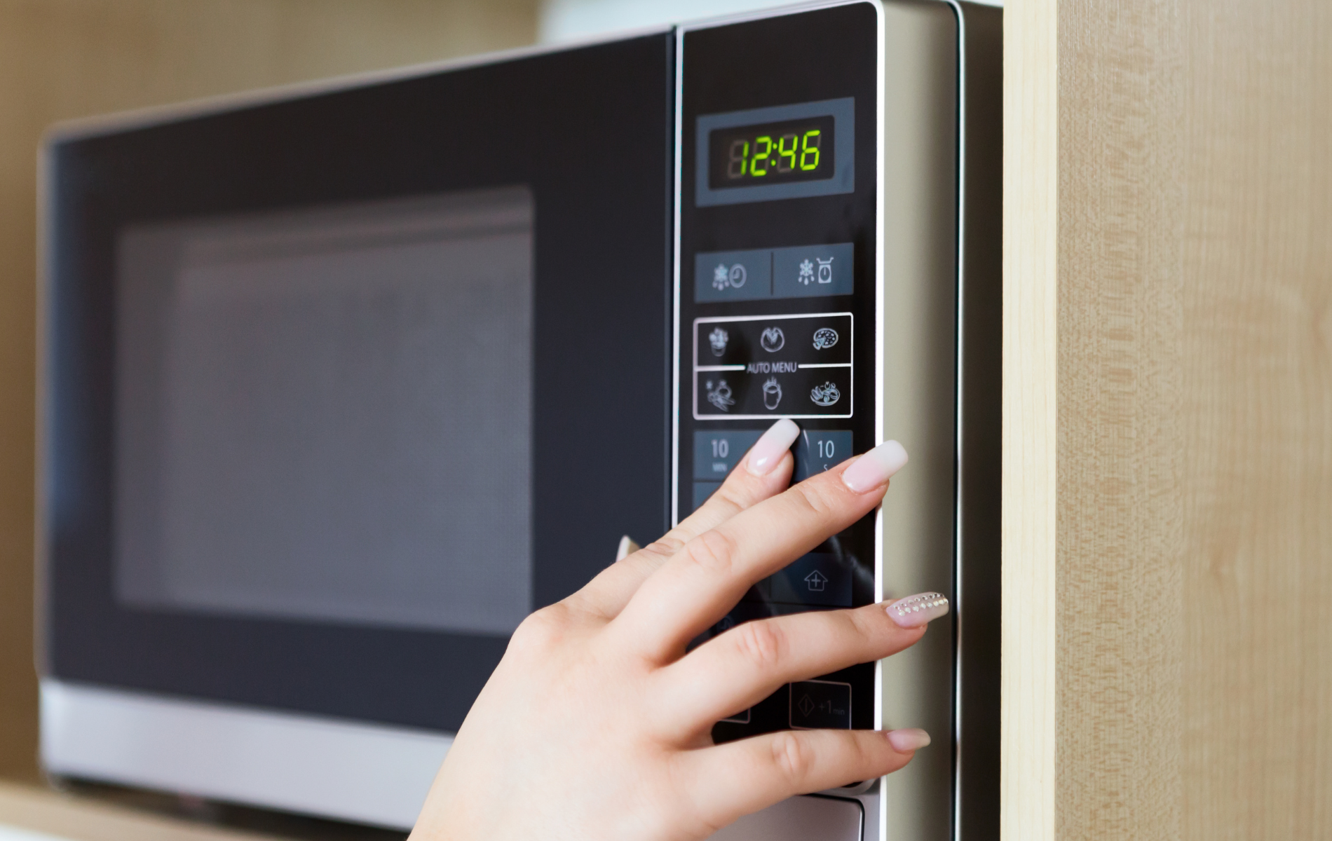 A woman 's hand is pressing a button on a microwave.