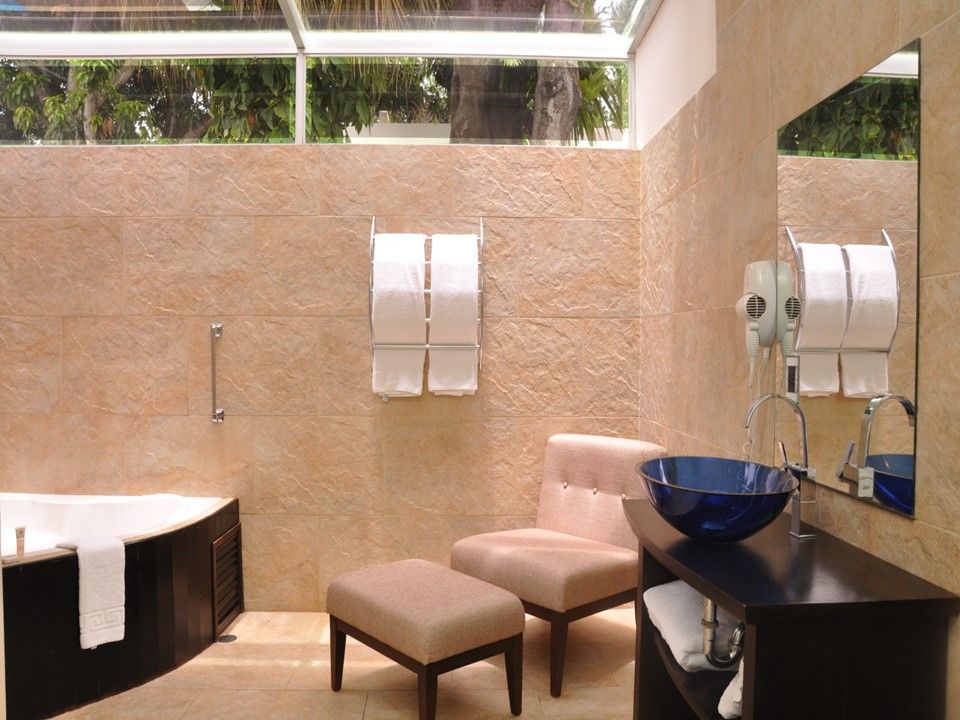 Un baño moderno con bañera, sillón con reposapiés, tocador con lavabo de cristal azul y paredes de azulejos color beige.