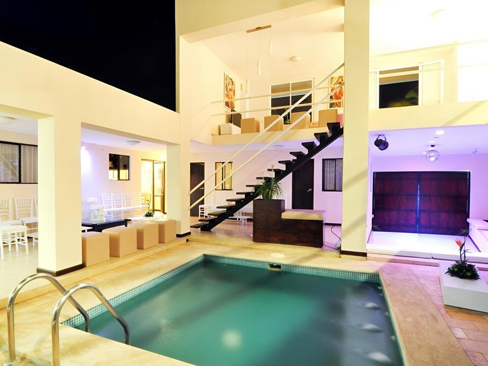 Una piscina al aire libre por la noche en el patio de una casa moderna de varios niveles con iluminación interior brillante.