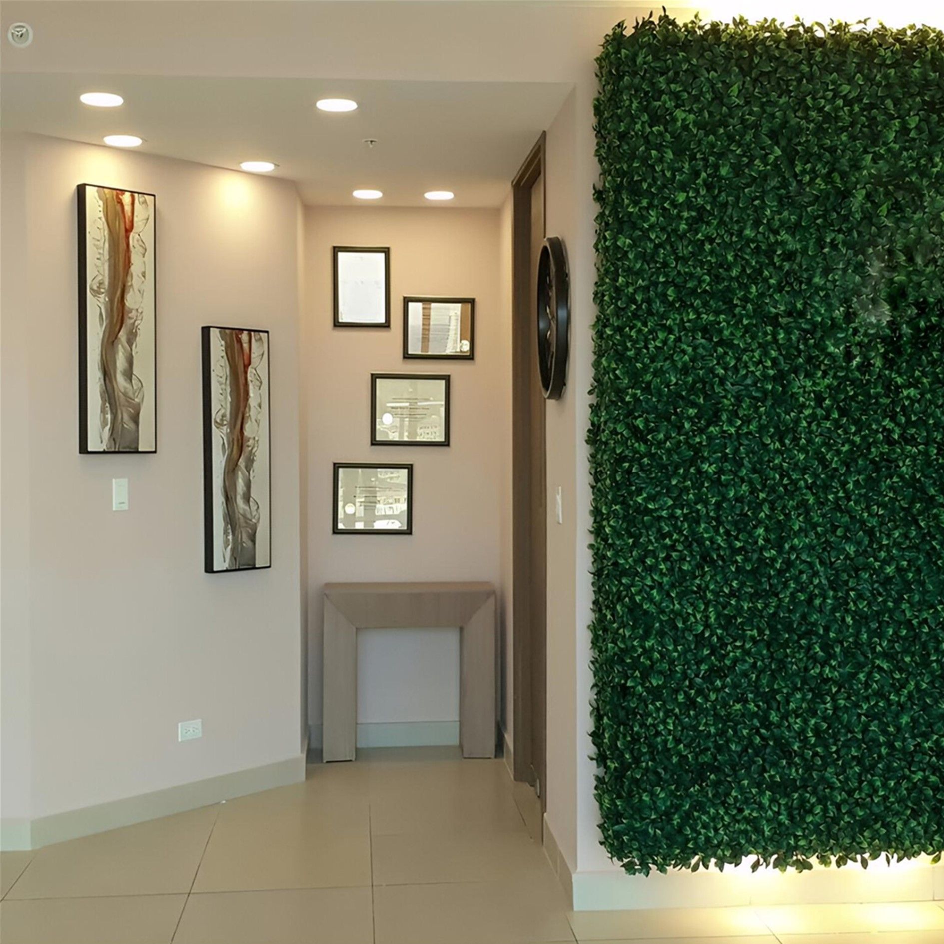 Un pasillo minimalista con paredes color crema, dos cuadros abstractos de gran tamaño, una pequeña mesa consola, marcos de fotos y una pared verde.