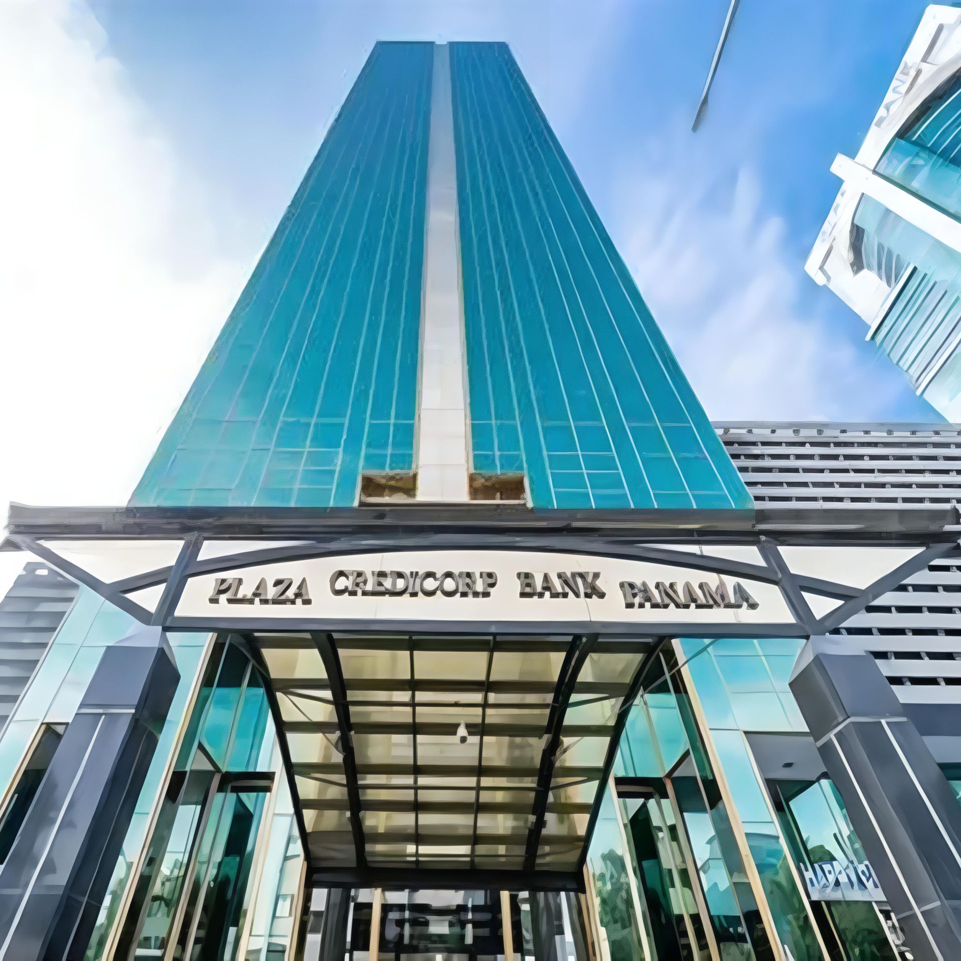 Vista desde un ángulo bajo de la torre Plaza Credicorp Bank Panama, de cristal color turquesa, con una prominente marquesina de entrada bajo un cielo azul.