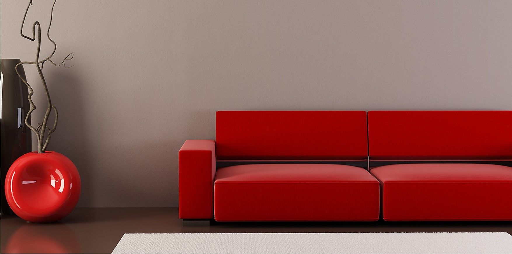 Un sofá de color rojo brillante se encuentra contra una pared lisa, junto a un jarrón circular rojo a juego con ramas decorativas.