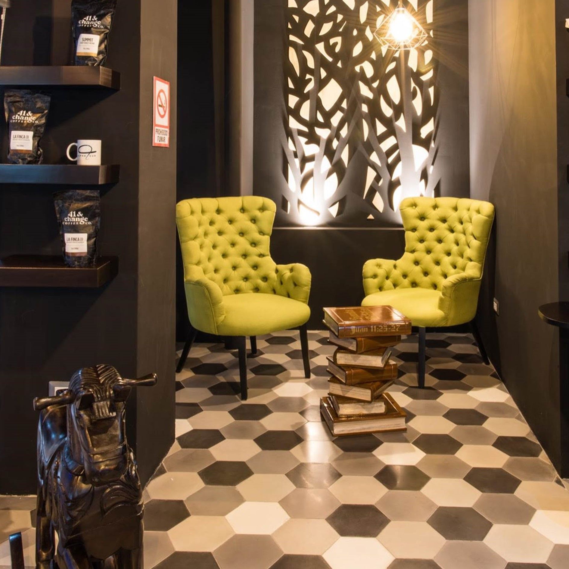 Dos sillones tapizados de color verde lima se encuentran uno frente al otro sobre un suelo de baldosas hexagonales, separados por una pila de libros que hace las veces de pequeña mesa.