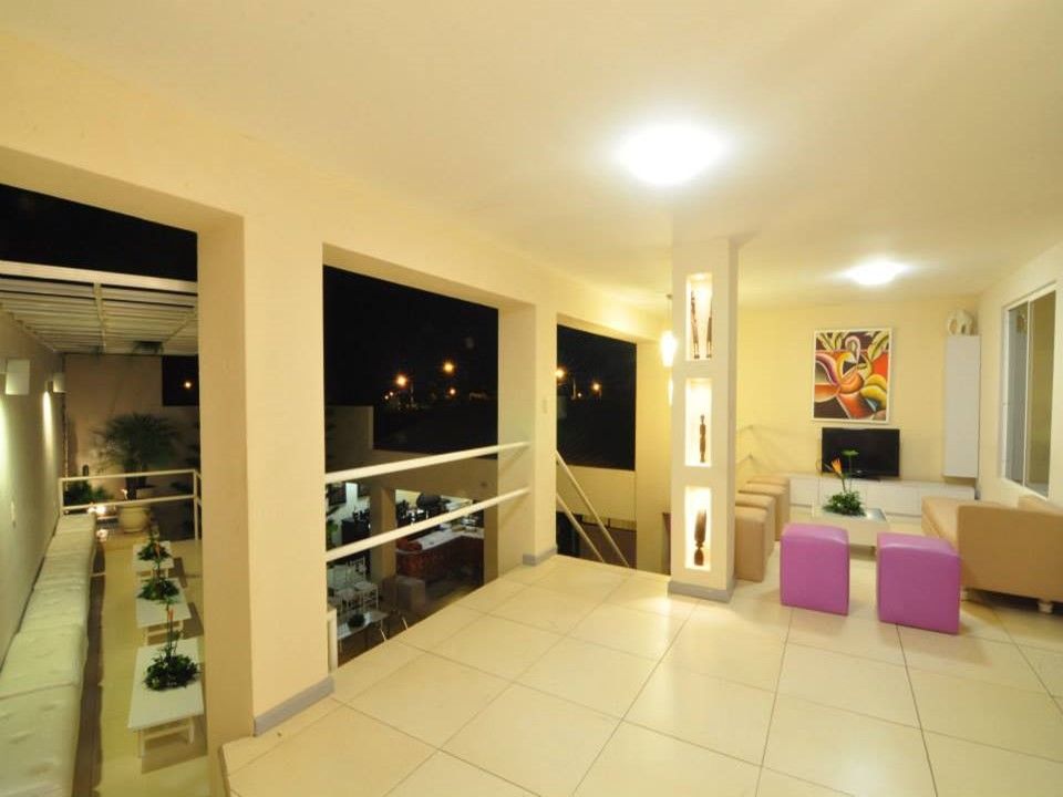 Un balcón interior luminoso y moderno con vistas a una planta inferior, con suelos de baldosas beige, muebles blancos y taburetes rosas.