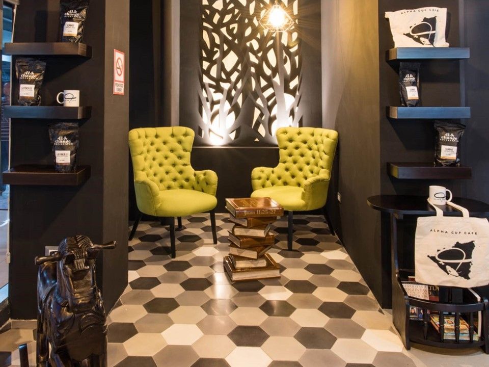 Dos sillones tapizados de color verde lima con una pila de libros a modo de mesa sobre un suelo de baldosas hexagonales en una cafetería moderna.