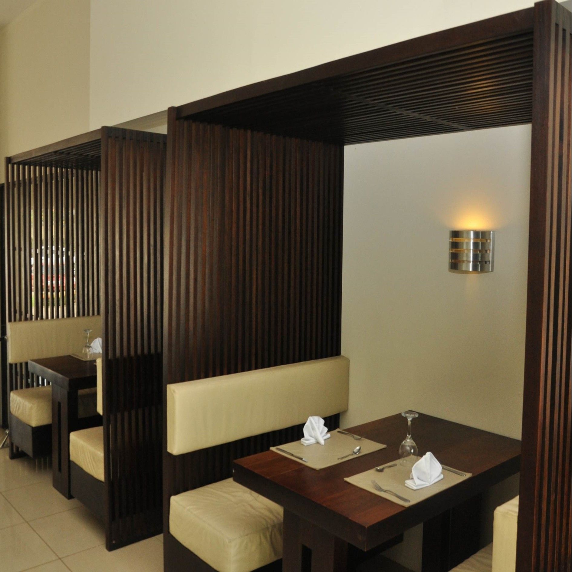 Dos reservados de restaurante con listones de madera oscura y asientos acolchados de color beige, con mesas dispuestas con servilletas y manteles individuales.