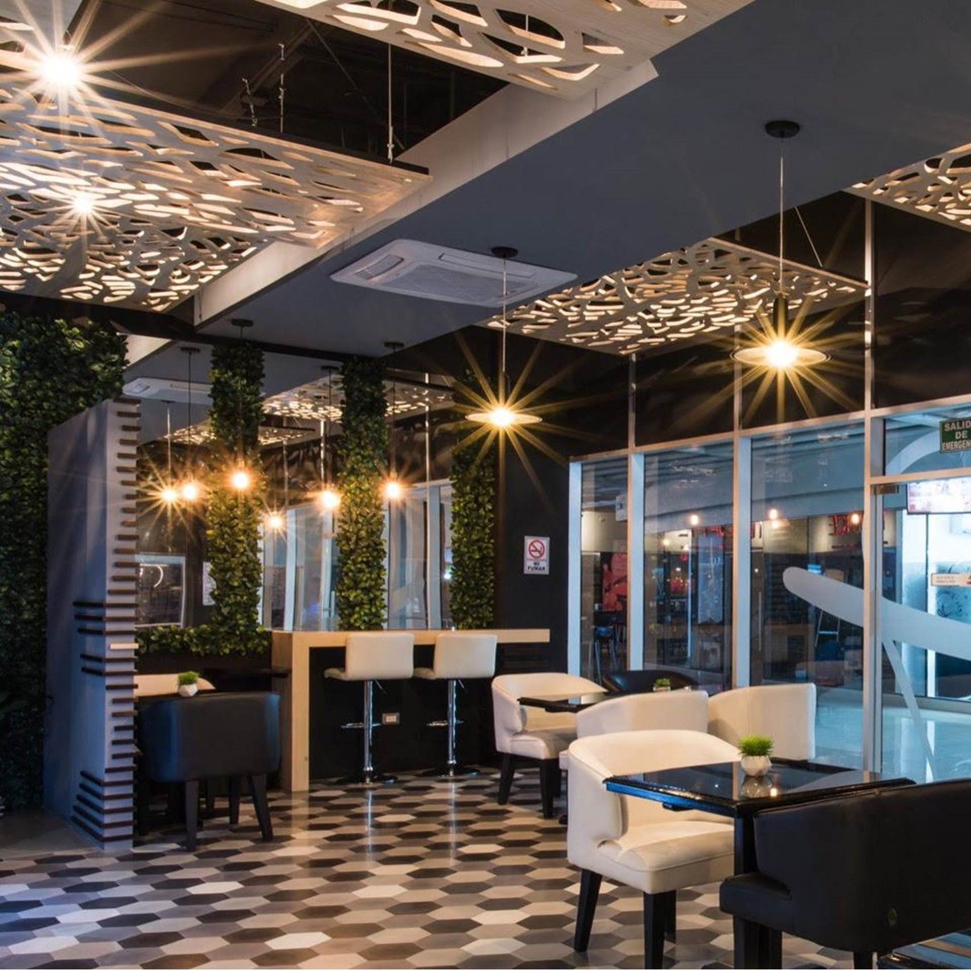 Interior de restaurante moderno con sillas blancas, taburetes oscuros en la barra, suelos con estampado hexagonal y paneles decorativos en el techo.