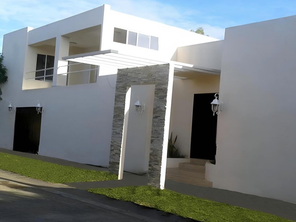 Una moderna casa blanca de dos plantas con una entrada con detalles de piedra, un balcón y un cuidado césped verde.
