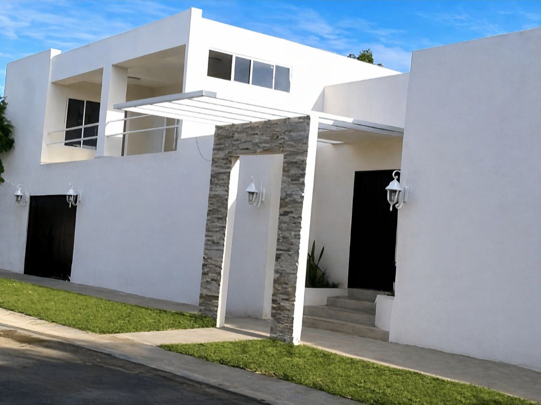 Una moderna casa blanca de dos plantas con una entrada con detalles de piedra, un balcón y un cuidado césped verde.