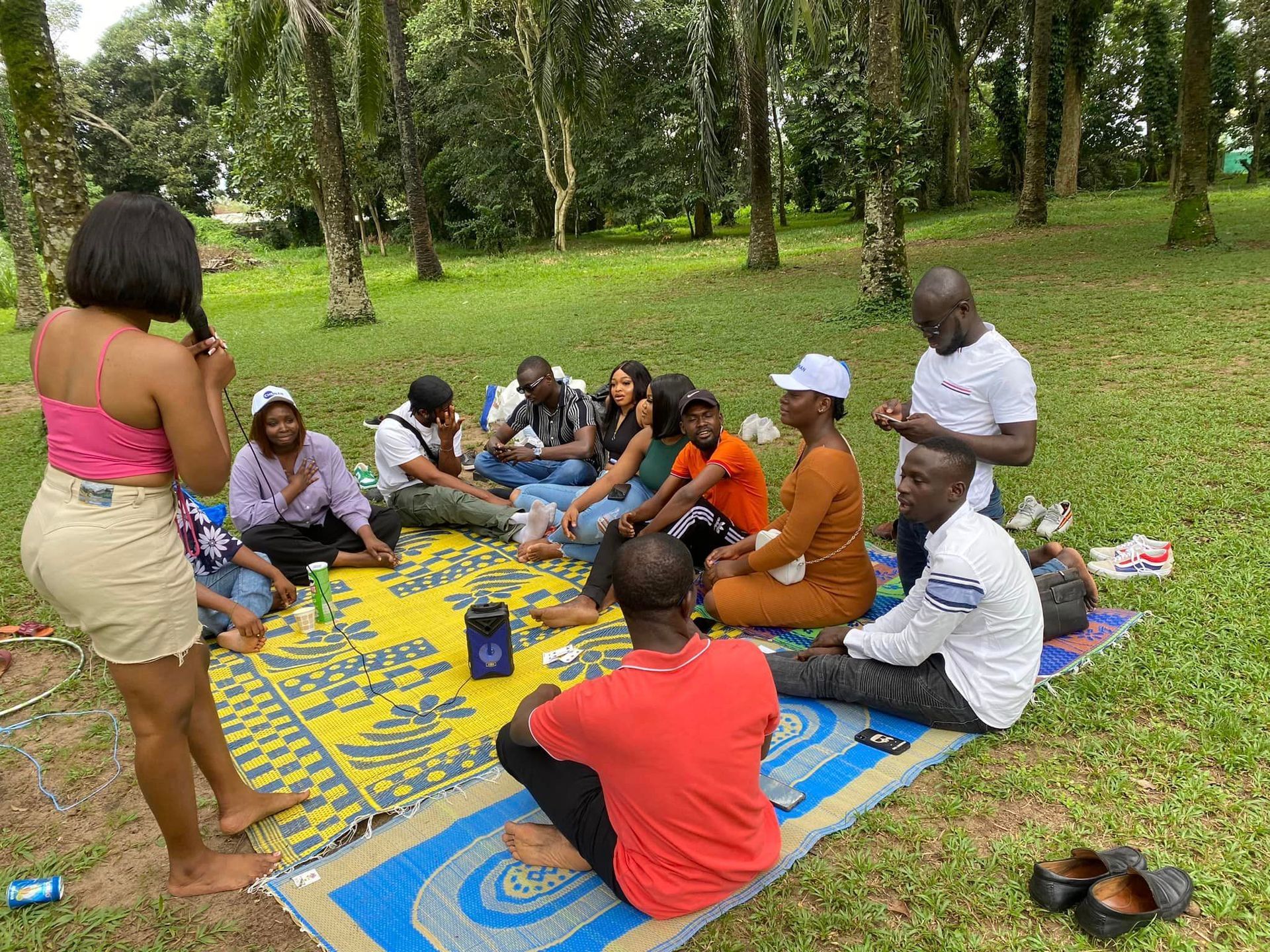 Un groupe de personnes pique-nique sur une couverture dans un parc, profitant de conversations et de nourriture.