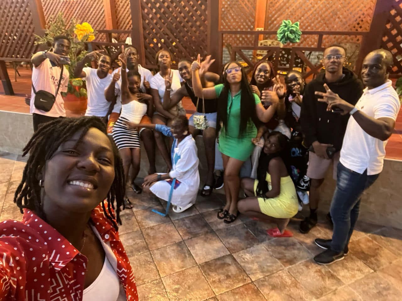 Groupe de personnes posant à l'extérieur, souriant et faisant signe de la main, éclairage chaleureux, terrasse en briques.