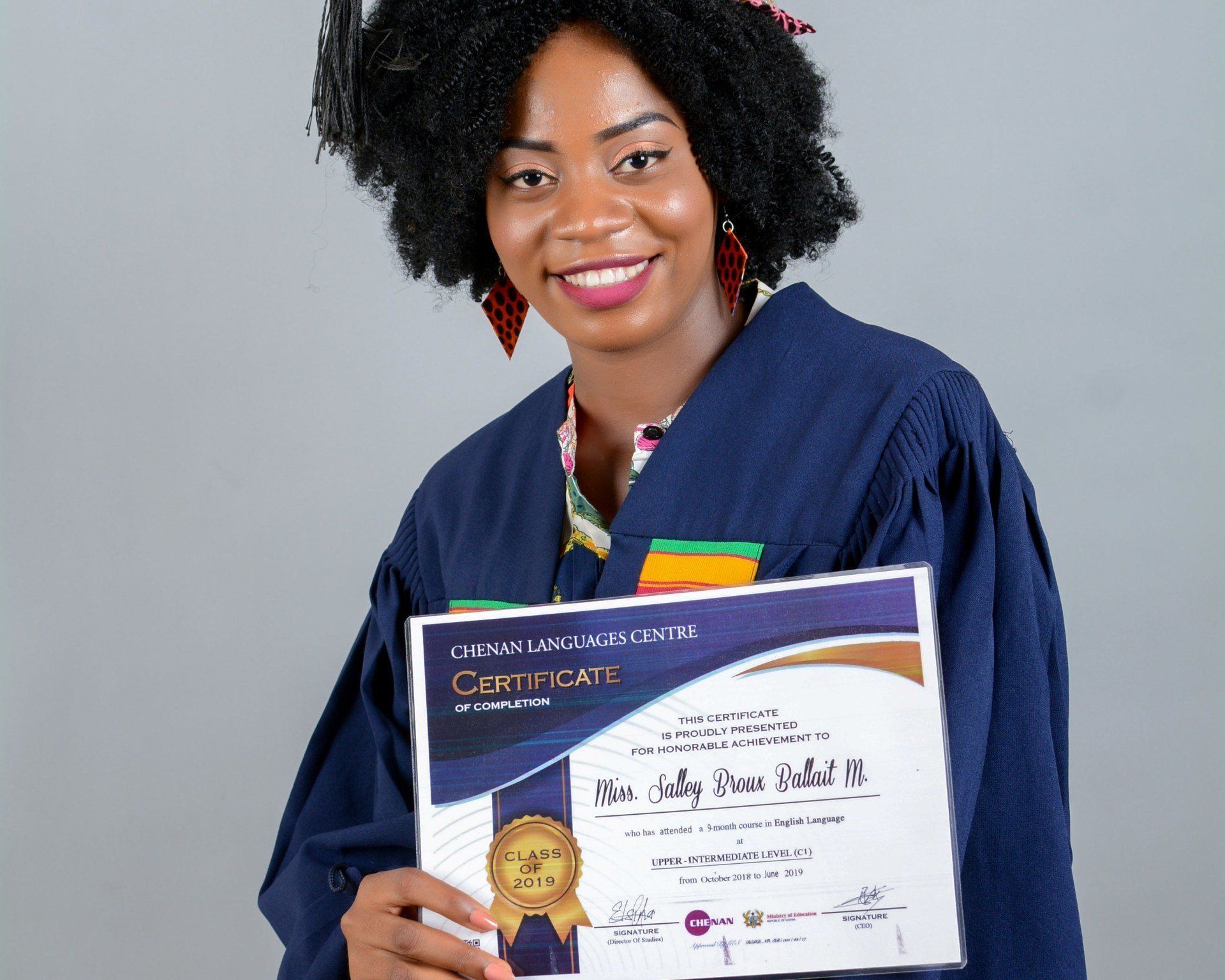 Femme en tenue de remise de diplôme, tenant un certificat et souriante.