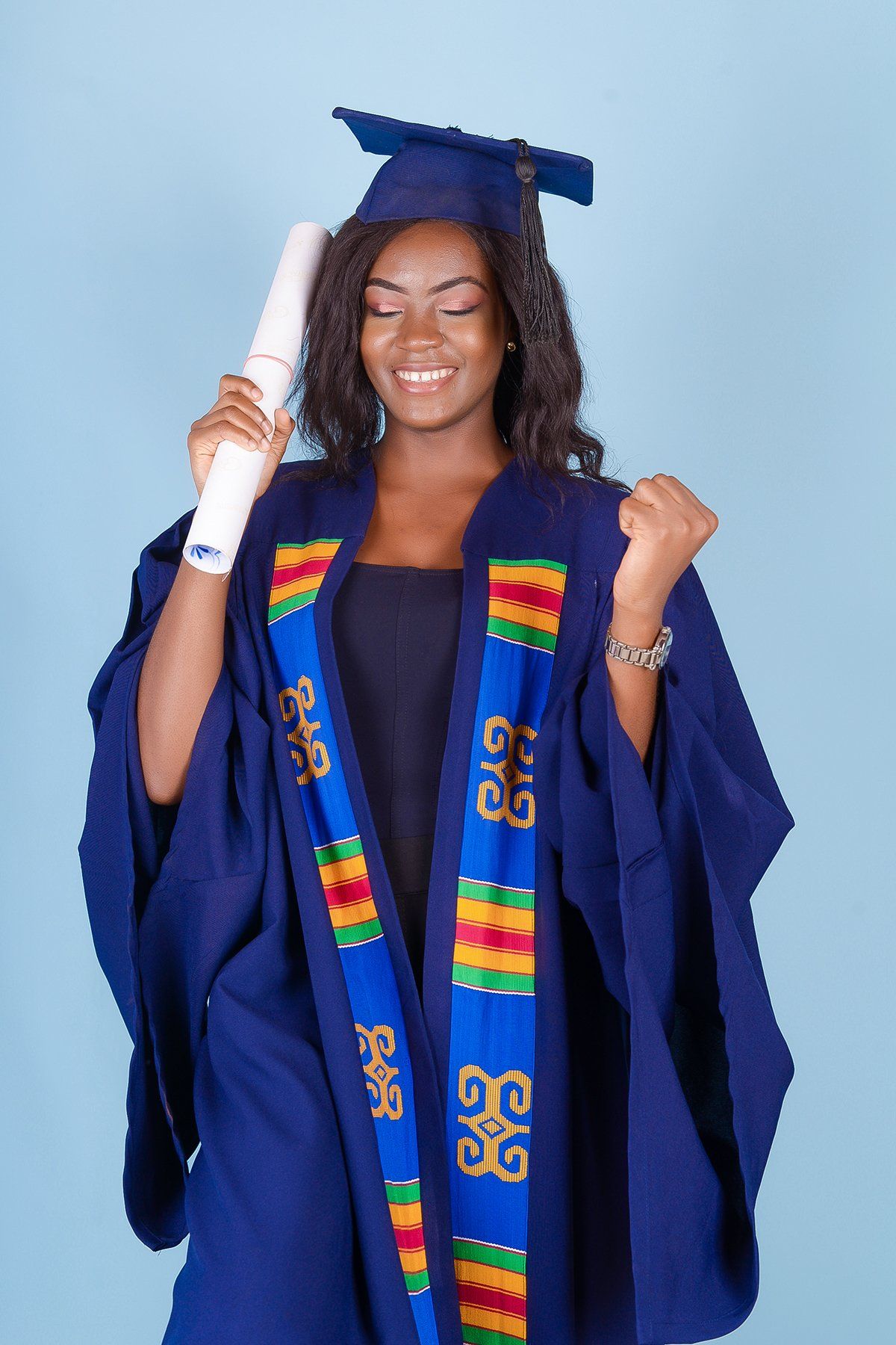 Femme en toge de remise de diplôme, tenant son diplôme, souriante et célébrant. Fond bleu.