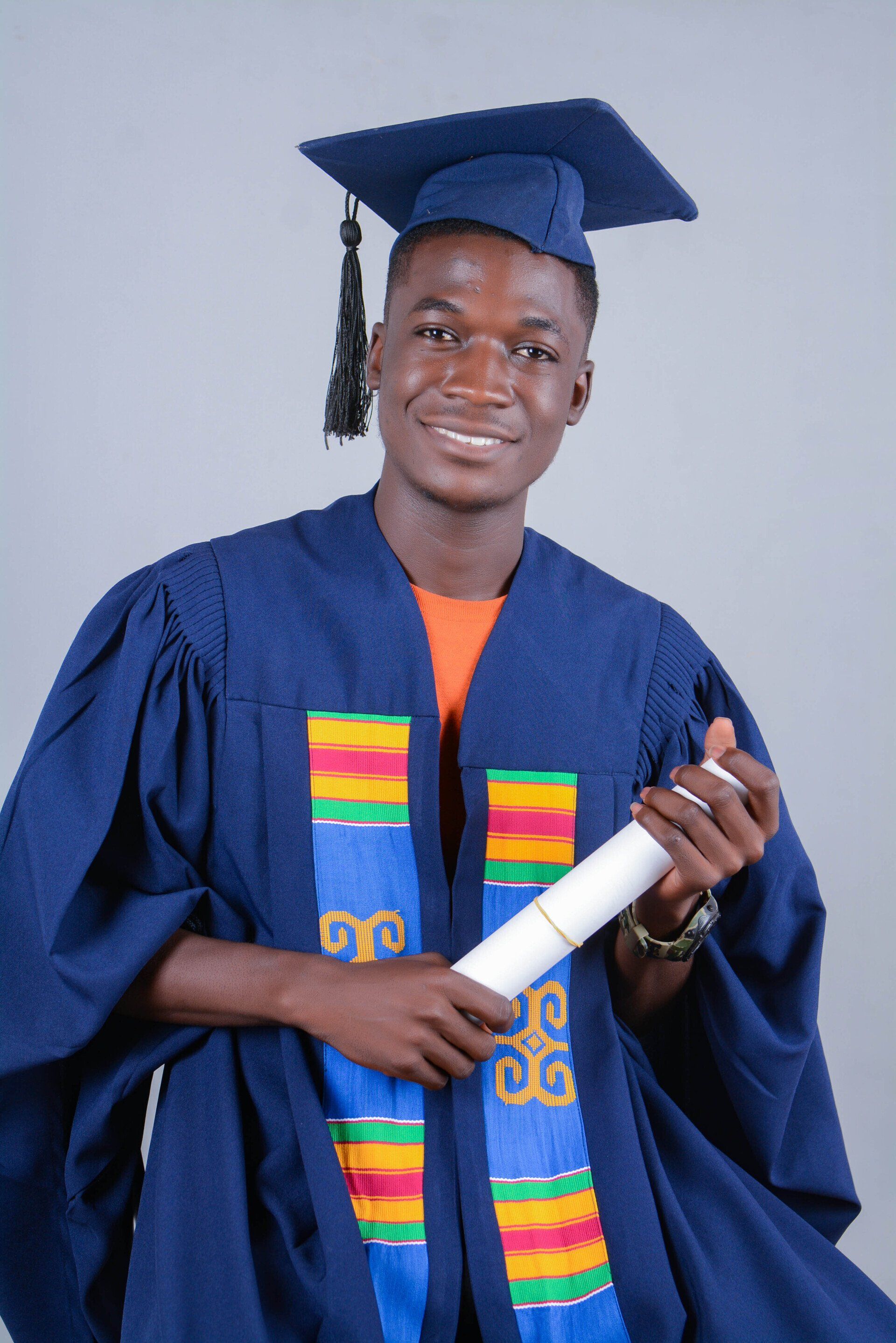 Homme en toge bleue tenant son diplôme, souriant. Fond gris.