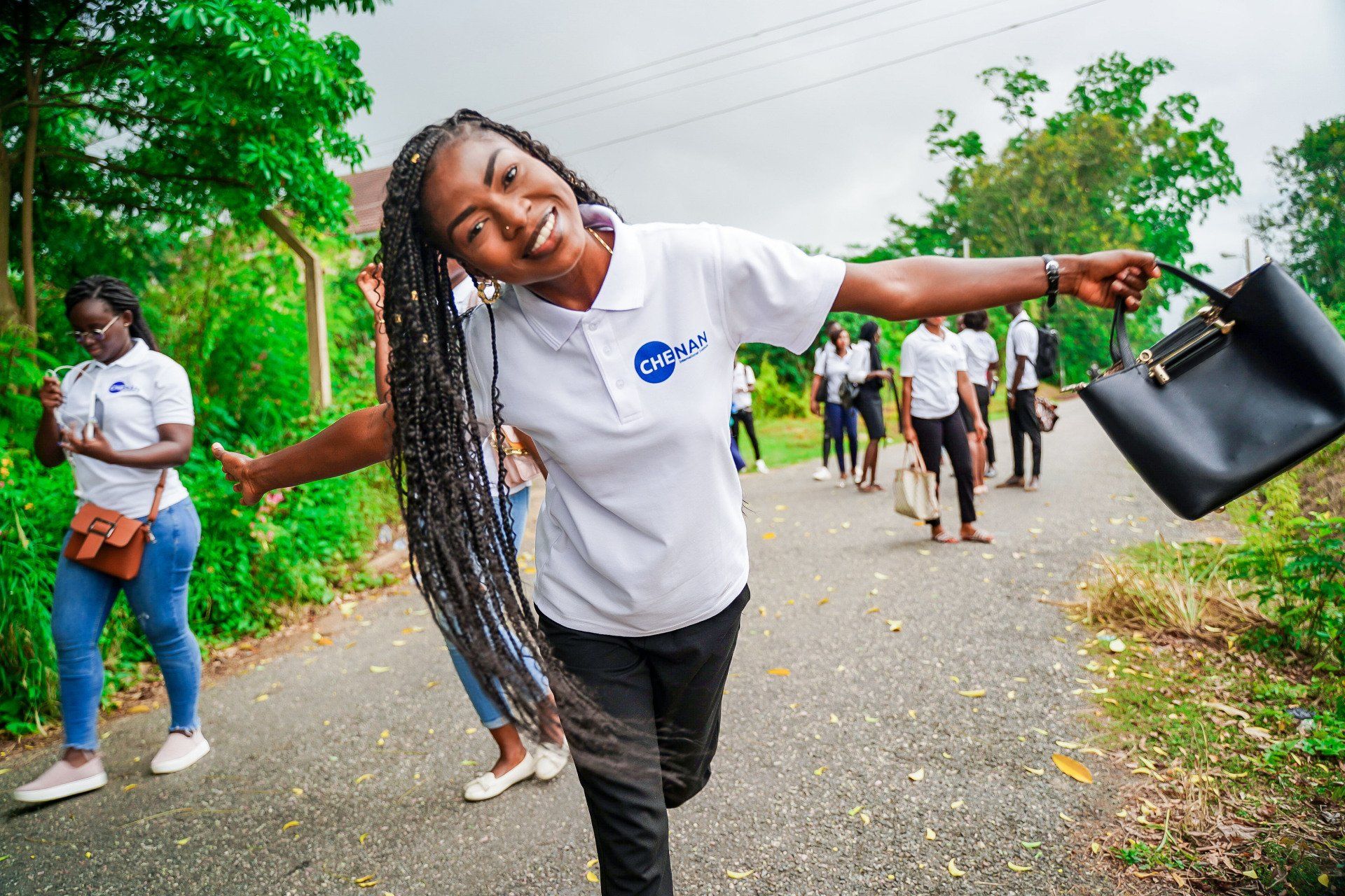 Une femme en chemise blanche tient un sac à main noir et sourit.