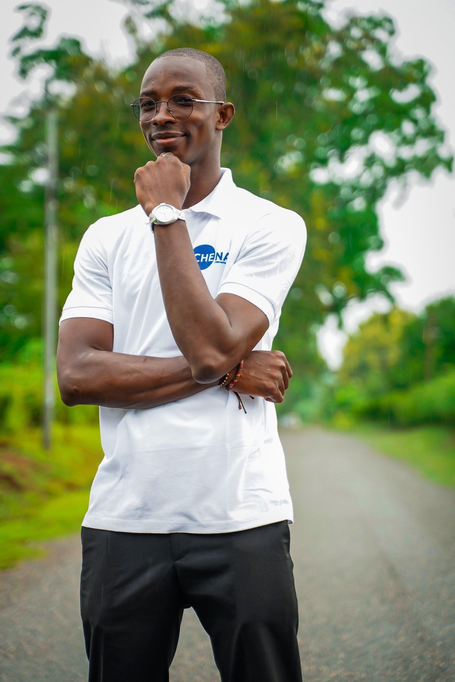 Un homme vêtu d'une chemise blanche et d'un pantalon noir est debout, les bras croisés et la main sur le menton.