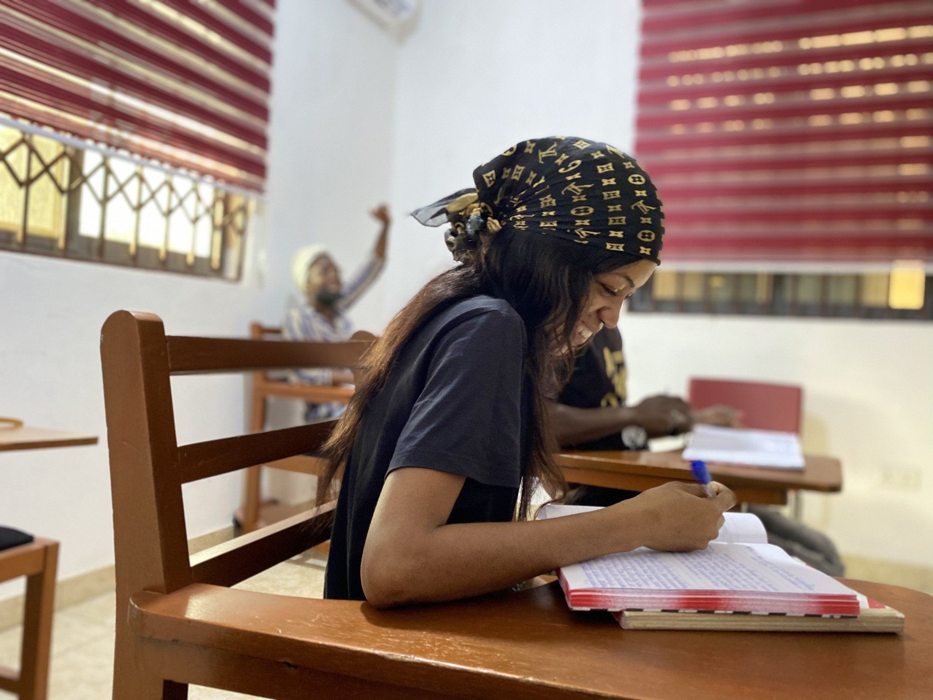 Une apprenante de Chenan Africa est assise à un bureau dans une salle de classe et écrit dans un cahier.