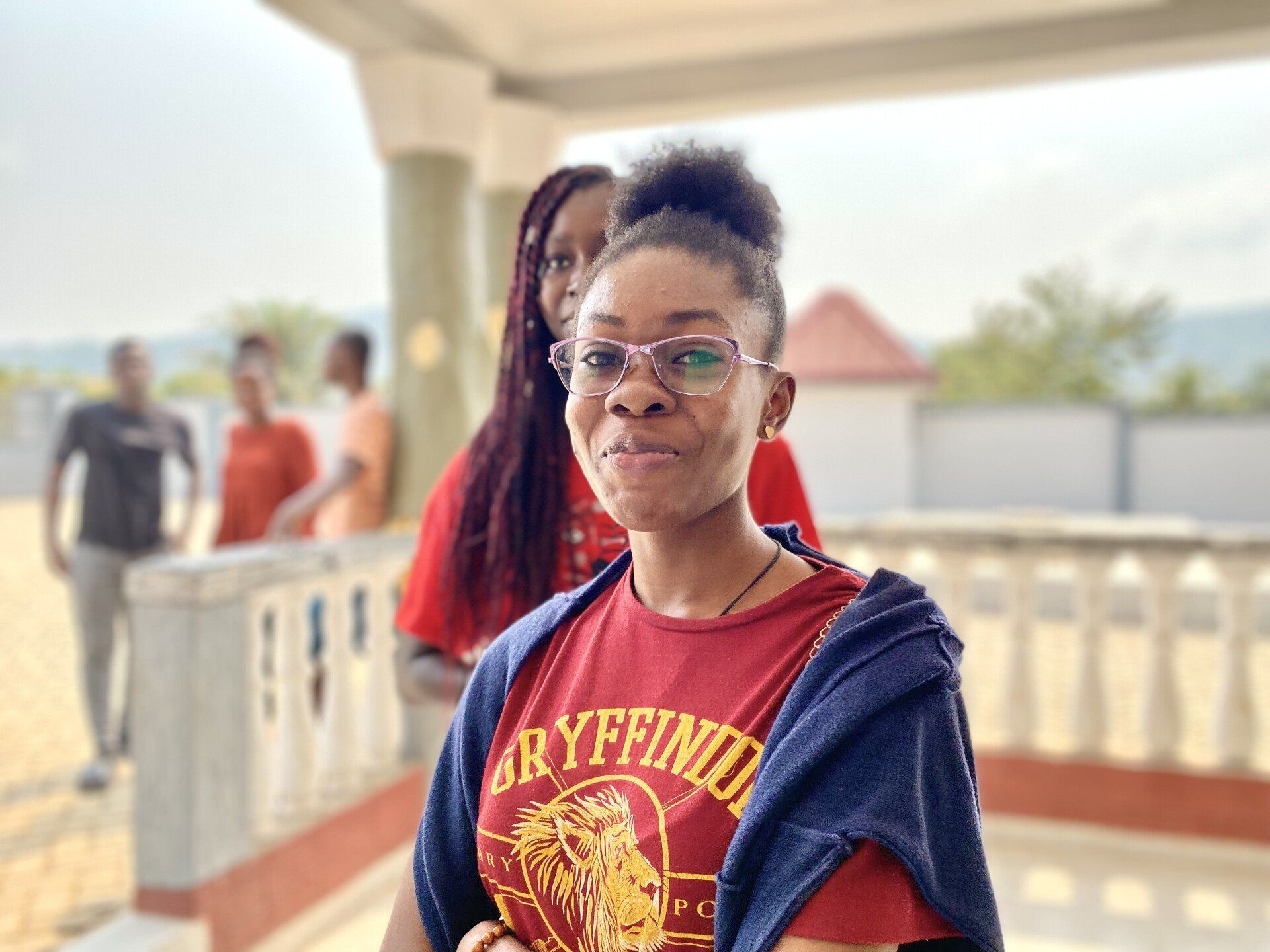 Une apprenante de Chenan Africa portant une chemise rouge de Gryffondor se tient sur un balcon.