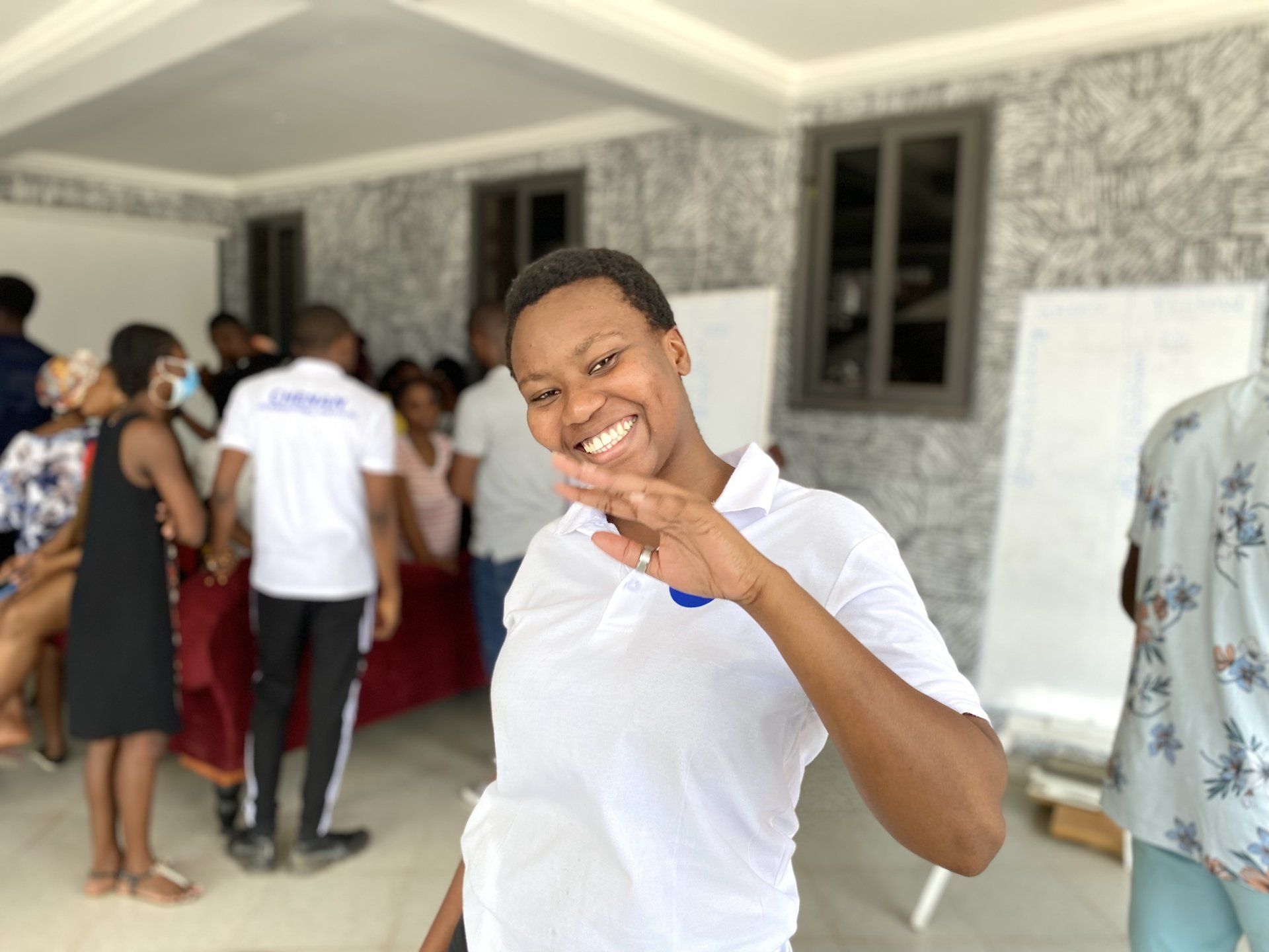 Une femme en chemise blanche sourit devant un groupe de personnes.