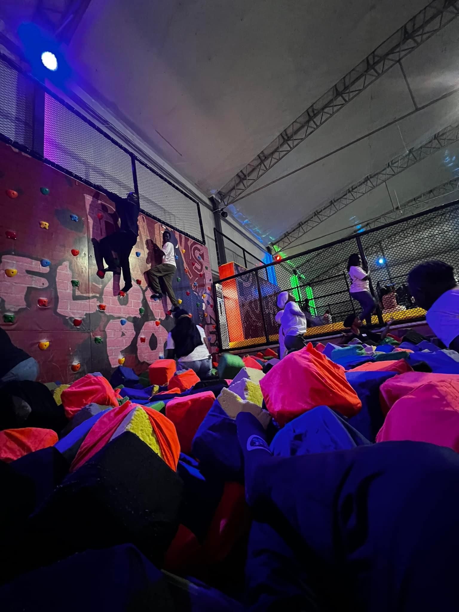 Des personnes escaladent un mur et jouent dans une fosse à mousse dans une aire de loisirs intérieure.