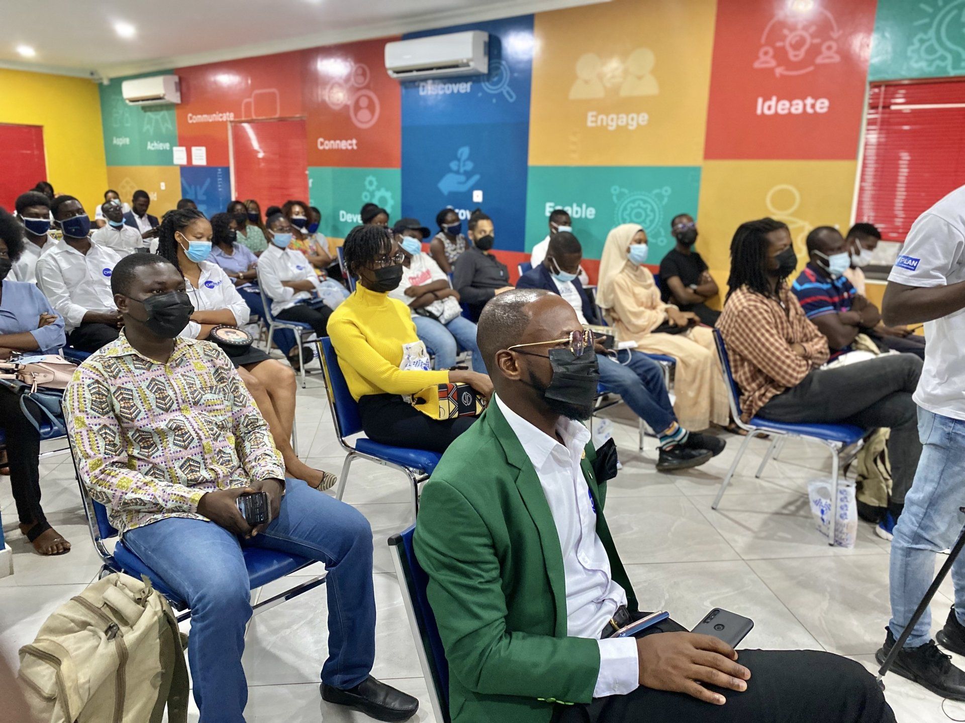 Un groupe de personnes portant des masques sont assises sur des chaises dans une pièce.