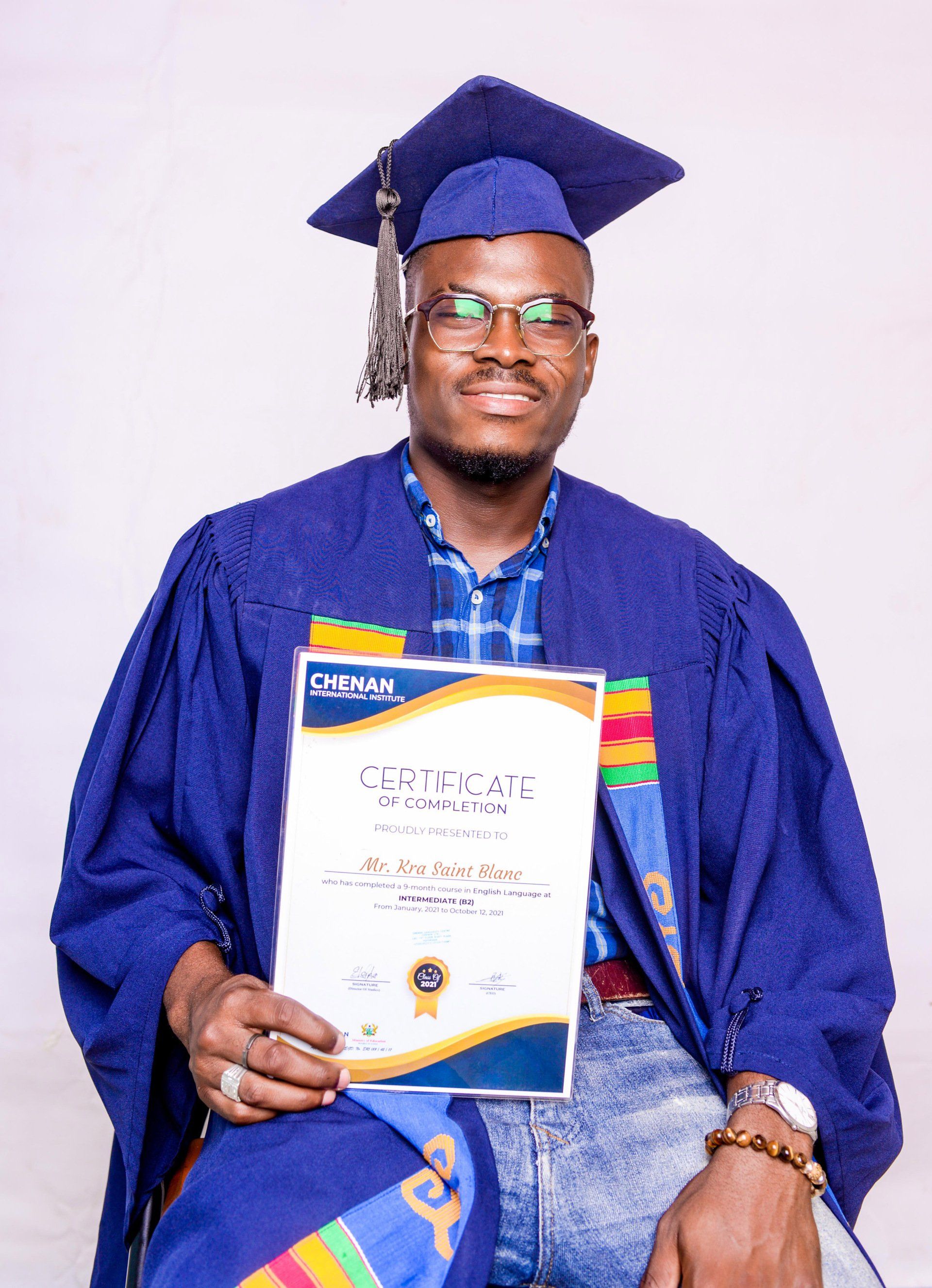 Un homme portant une casquette et une robe de graduation tient un certificat.