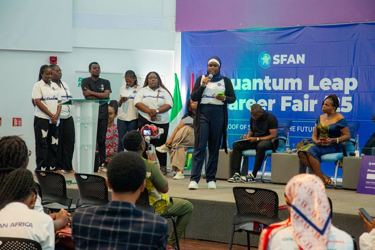 Des personnes se trouvent sur une scène lors d'un forum de l'emploi. L'une d'elles parle au micro. Plusieurs autres se tiennent derrière elle.