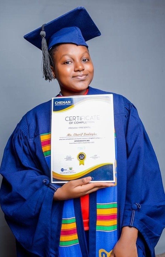 Une femme portant une casquette et une robe de graduation tient un certificat.