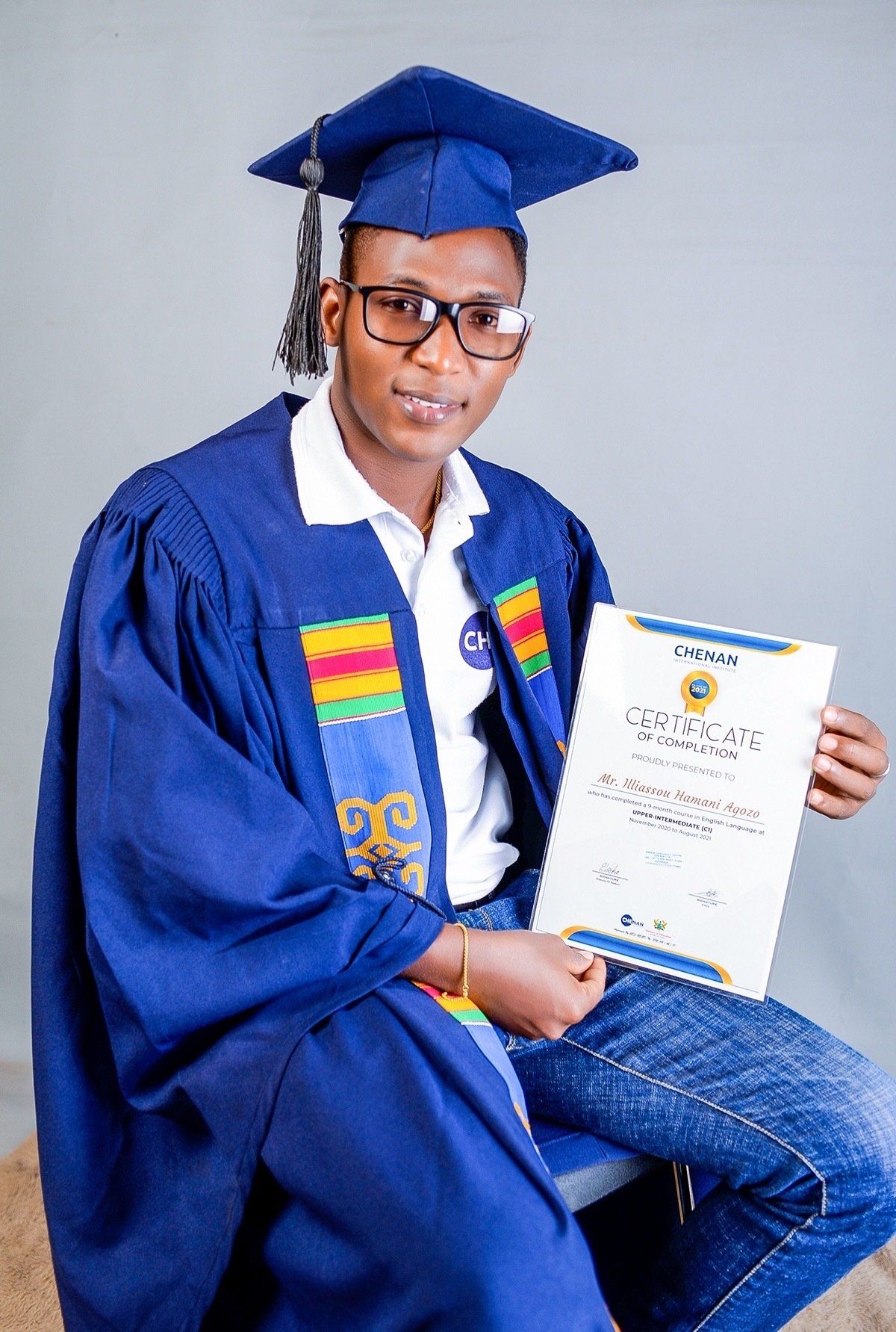 Un homme portant une casquette et une robe de graduation tient un certificat.