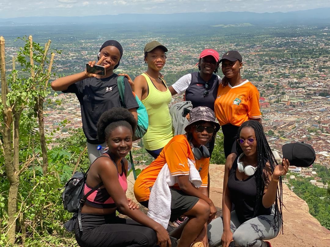 Groupe de personnes au sommet d'une colline, souriant et prenant la pose. Ville en arrière-plan. Journée ensoleillée.