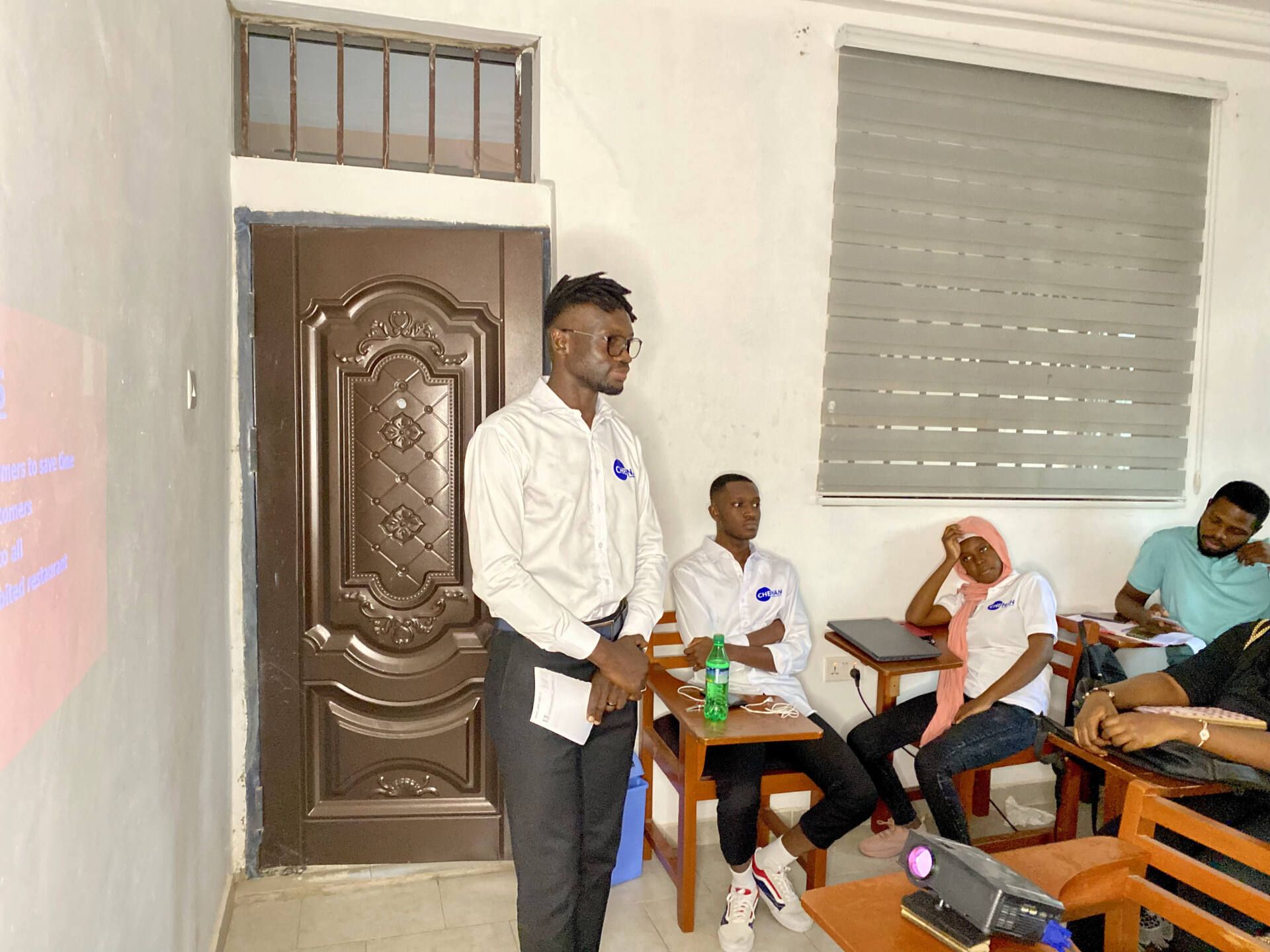 Un  apprenant de Chenan Africa fait une présentation à un groupe de personnes dans une salle de classe.