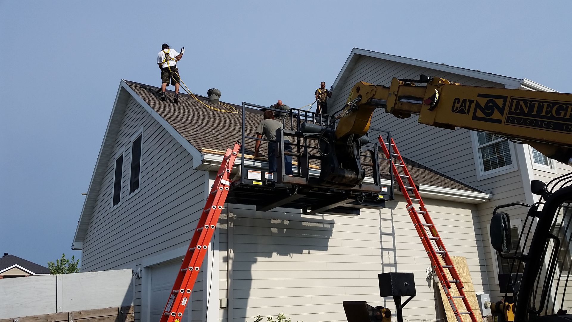 fiberglass shingles being torn off by roofers with hand tools, safety harnesses and ladders near the Fargo-Moorhead area
