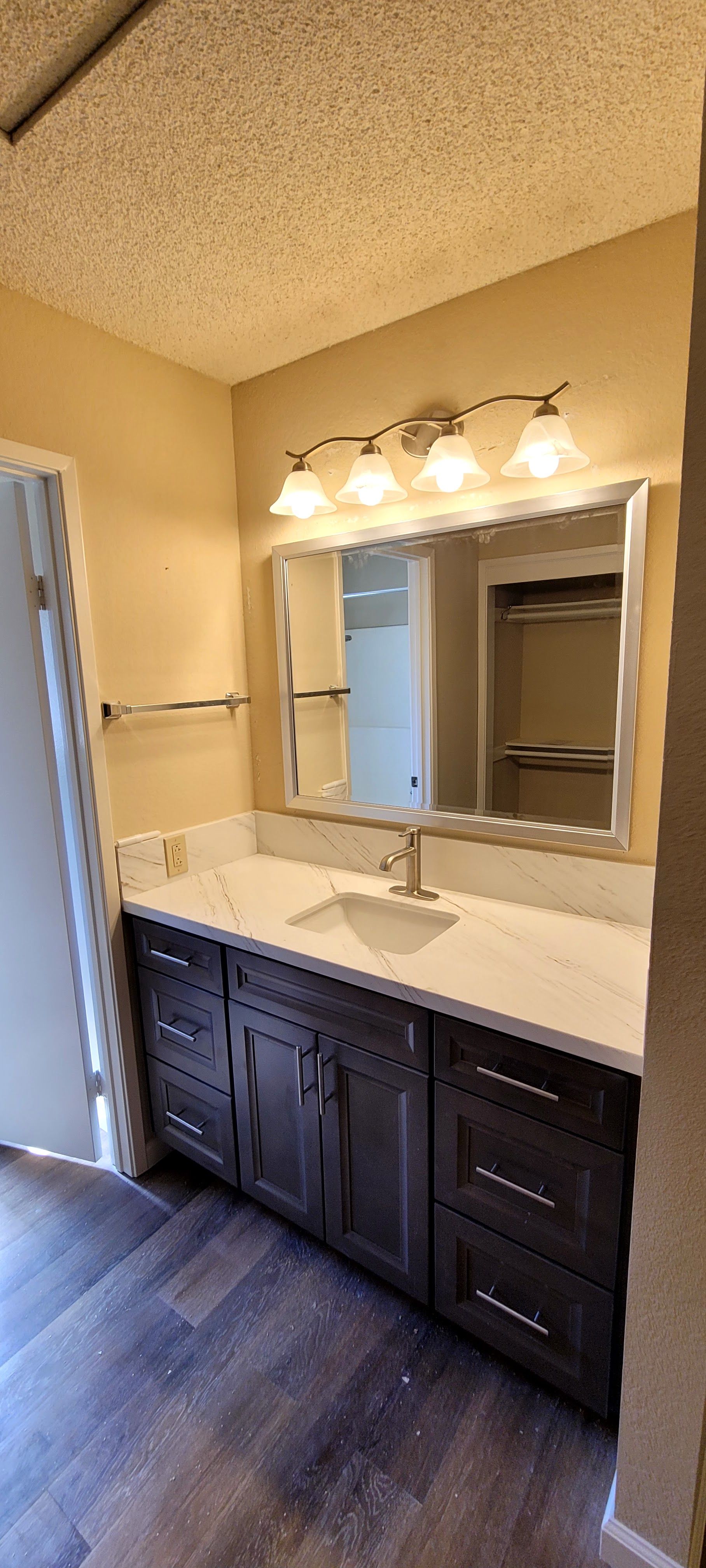 A modern bathroom vanity with dark wood cabinets, a white countertop, a rectangular mirror, and four-bulb light fixture.