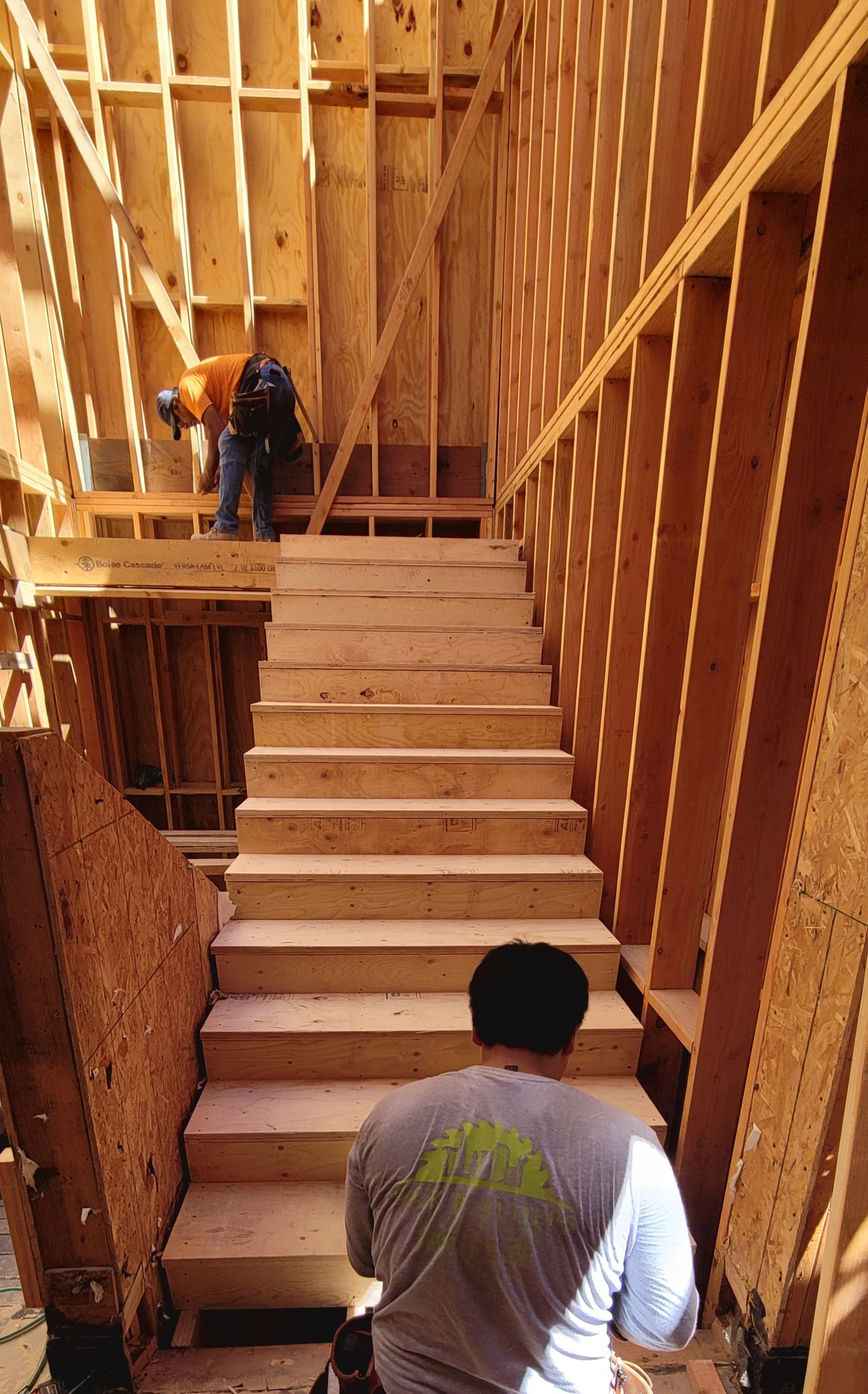 Two construction workers install wooden stairs within the exposed timber framing of a building under construction.