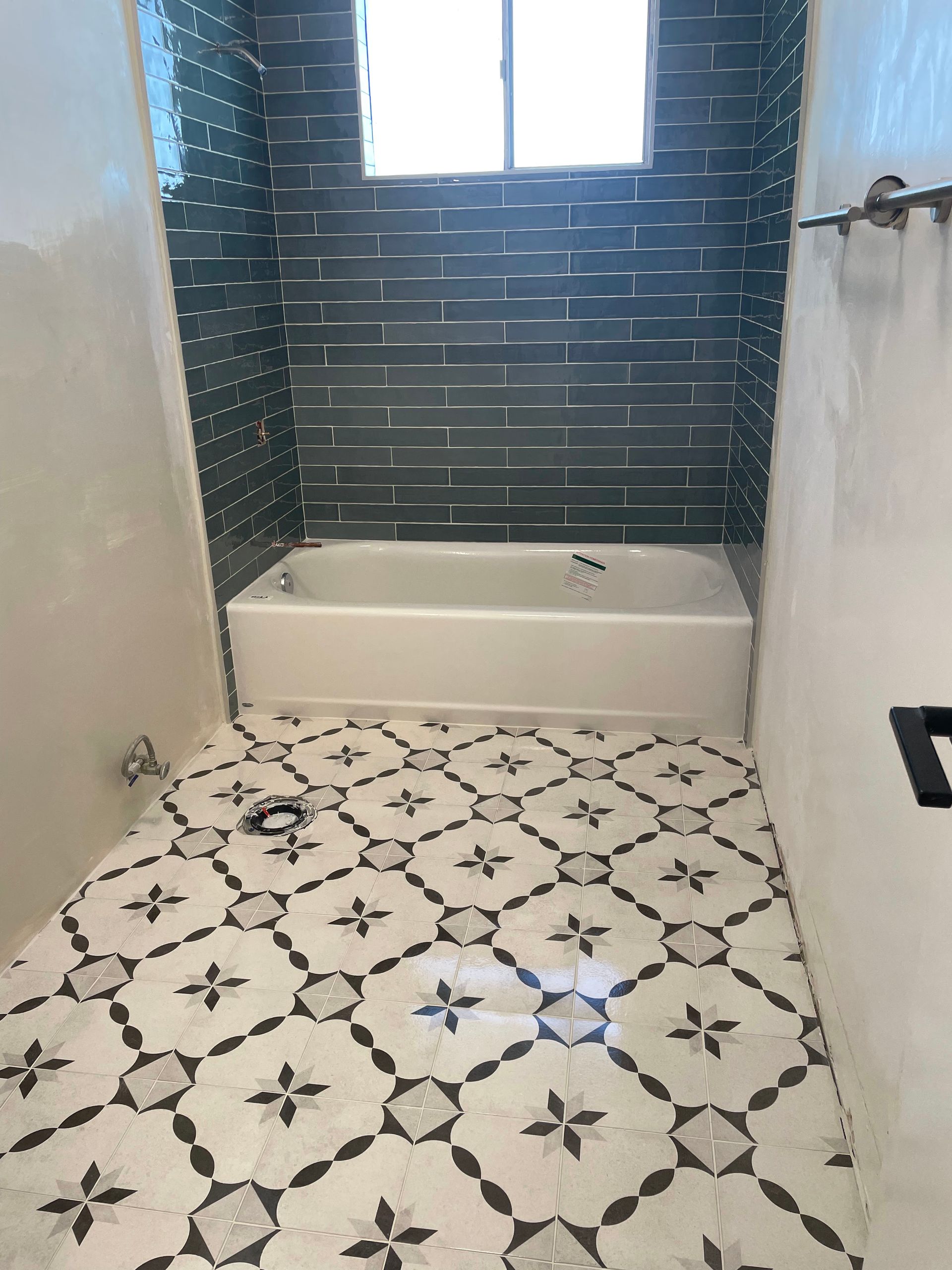 A bathroom with a white bathtub, dark blue subway tile on the back wall, and patterned white and gray floor tiles.