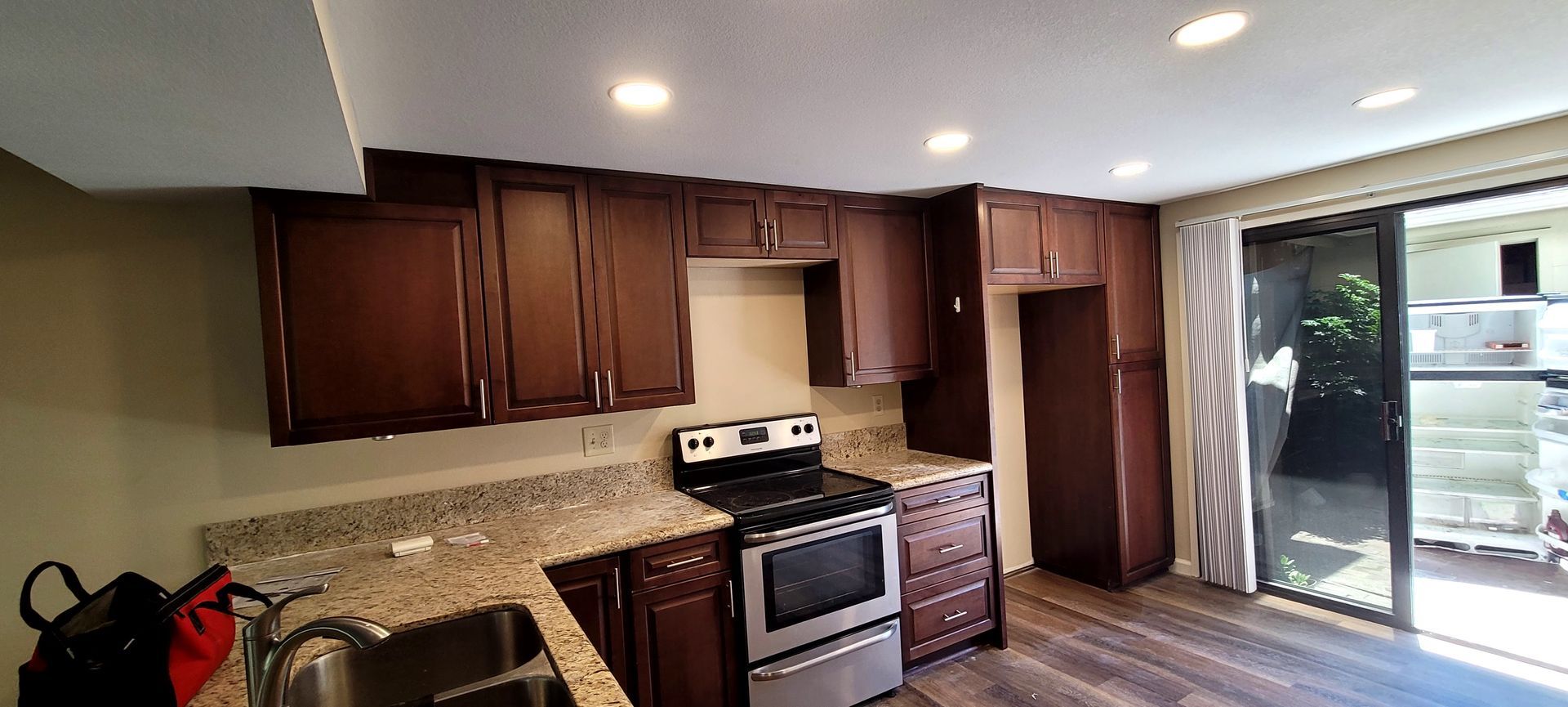 A kitchen featuring dark wood cabinets, granite countertops, stainless steel appliances, and a glass sliding door.
