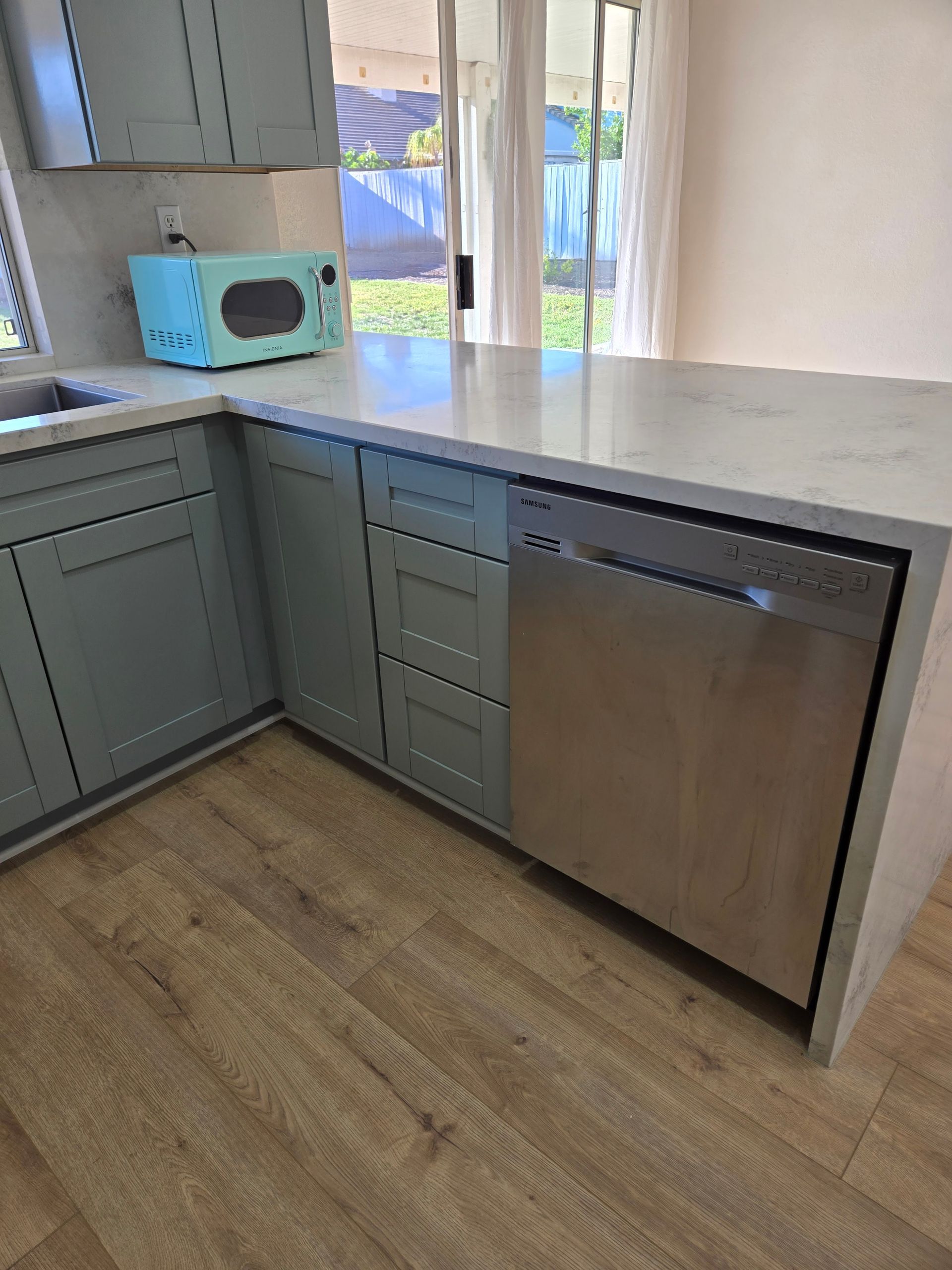 A kitchen corner with gray cabinets, a light-blue microwave on the counter, and a stainless steel dishwasher below.