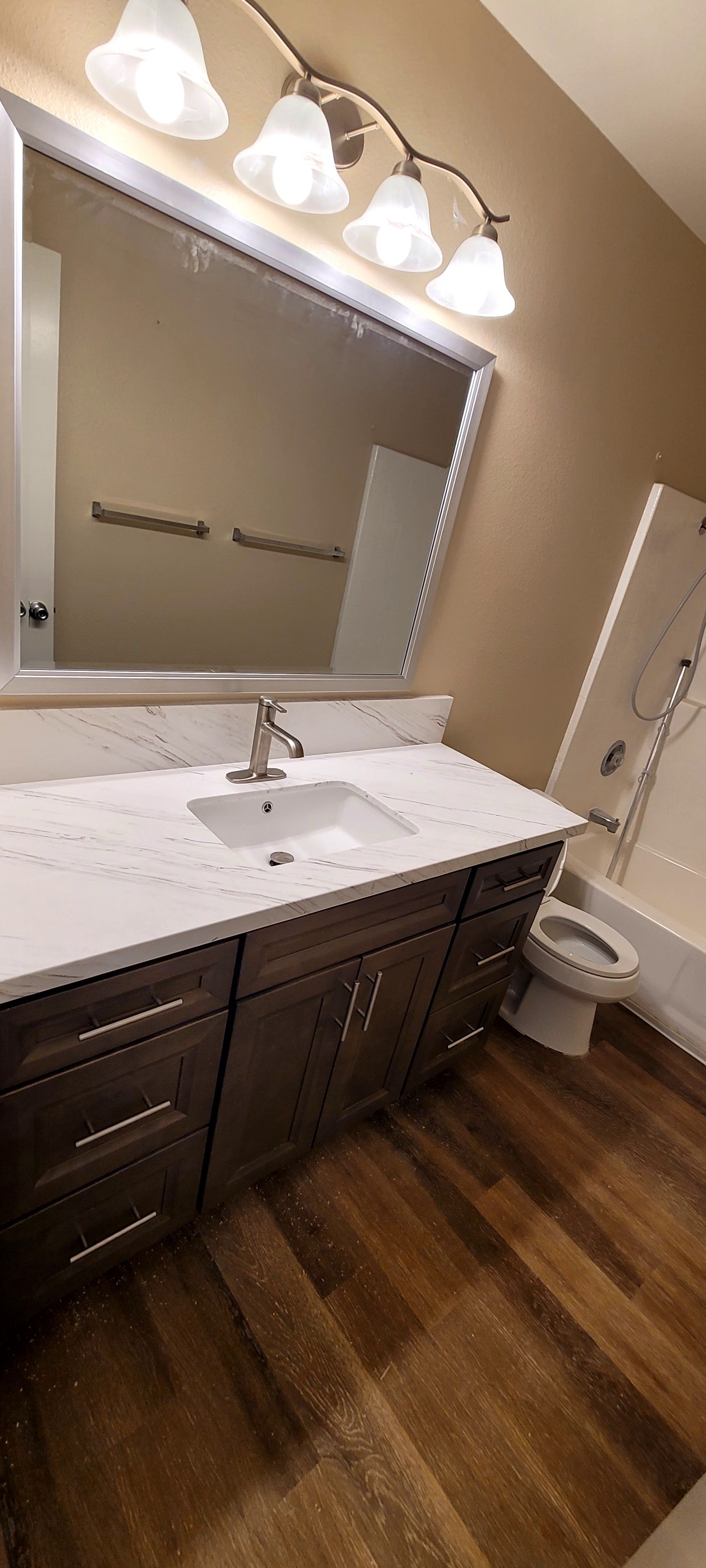 A modern bathroom with a dark wood vanity, white marble countertop, large rectangular mirror, and light wood-look flooring.