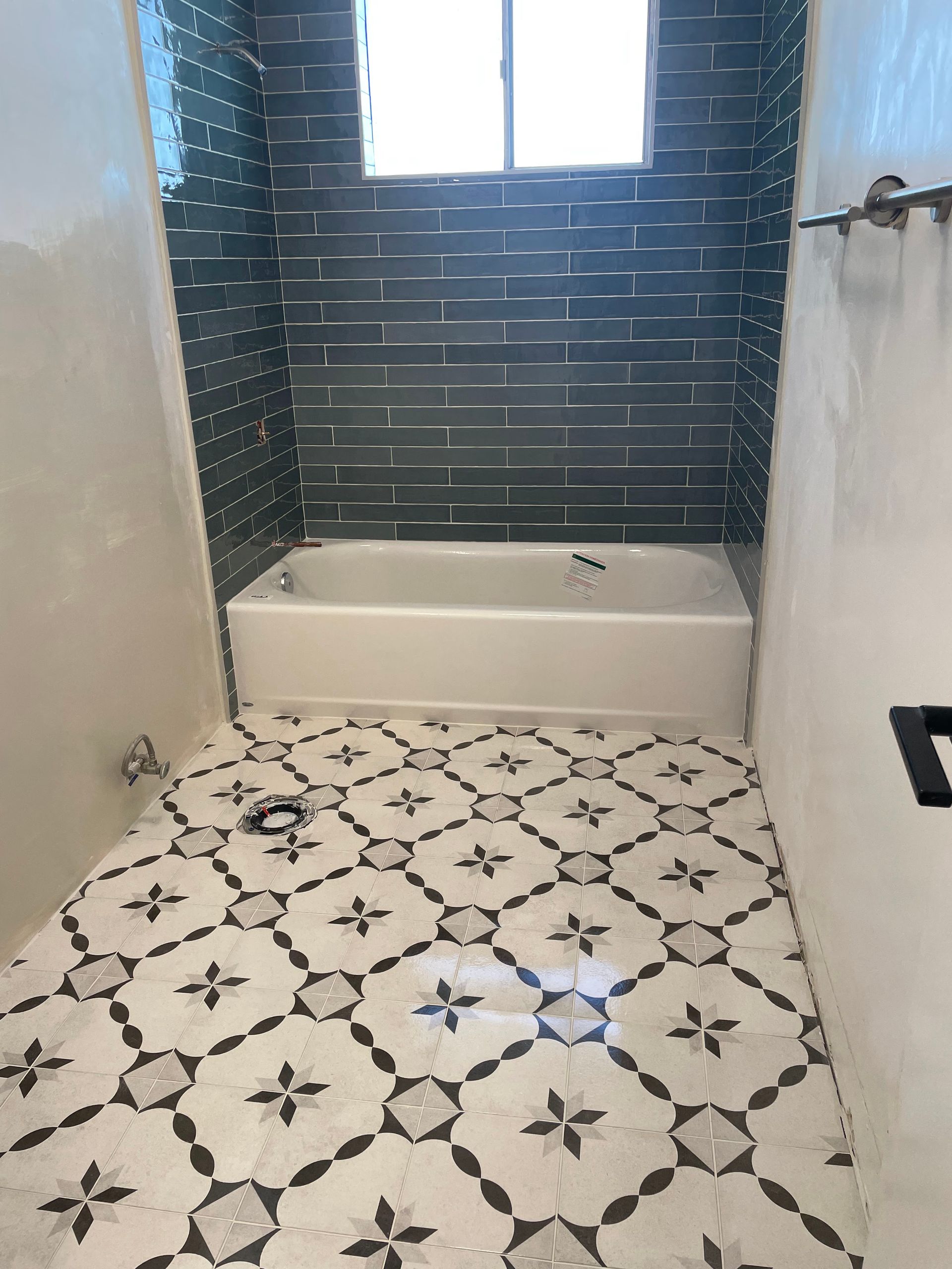 A bathroom with a white bathtub, dark blue subway tile shower wall, and patterned white and black floor tiles.