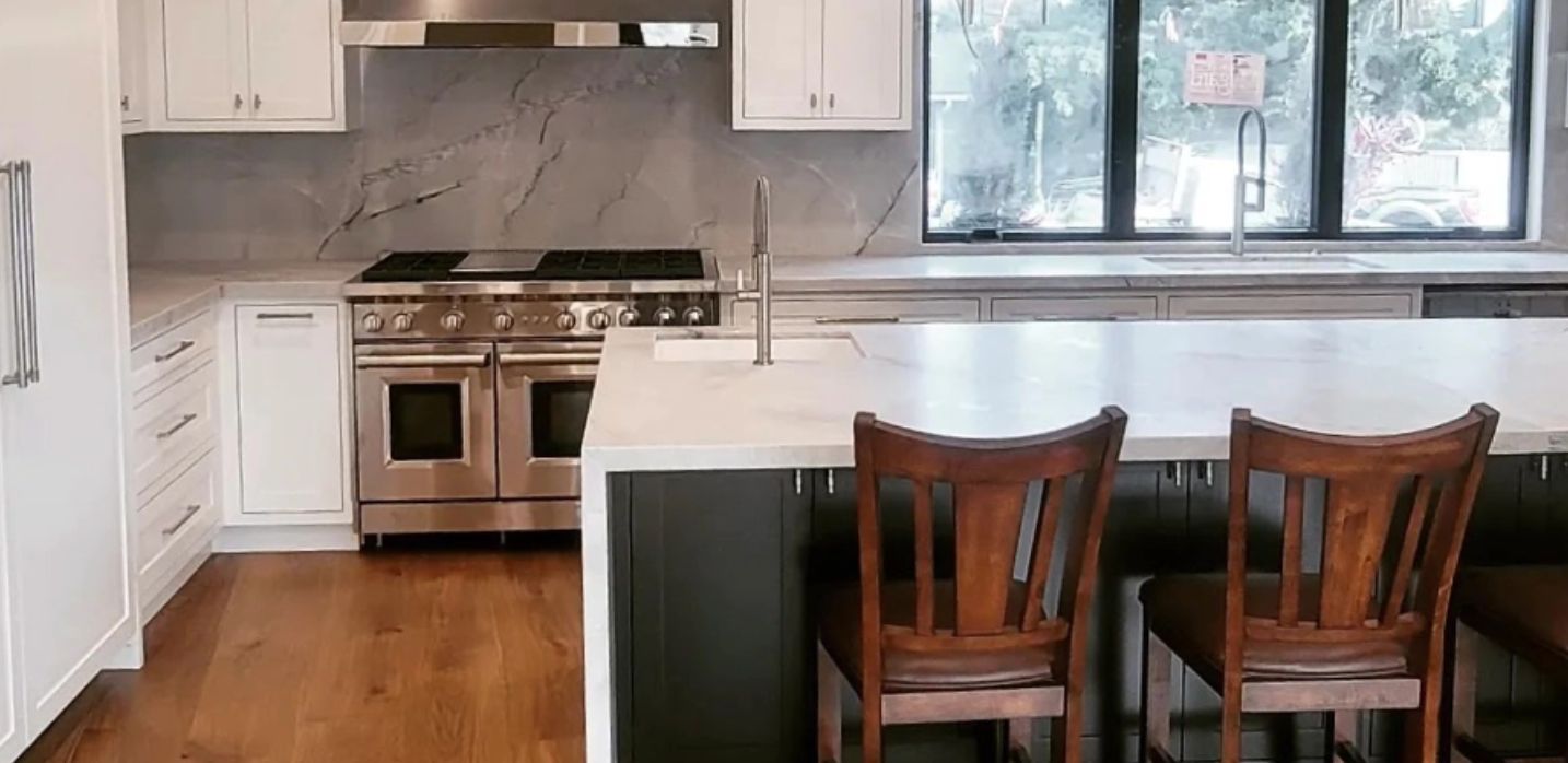 A modern kitchen with white cabinets, marble backsplash, stainless steel range, and two dark wooden chairs at an island.