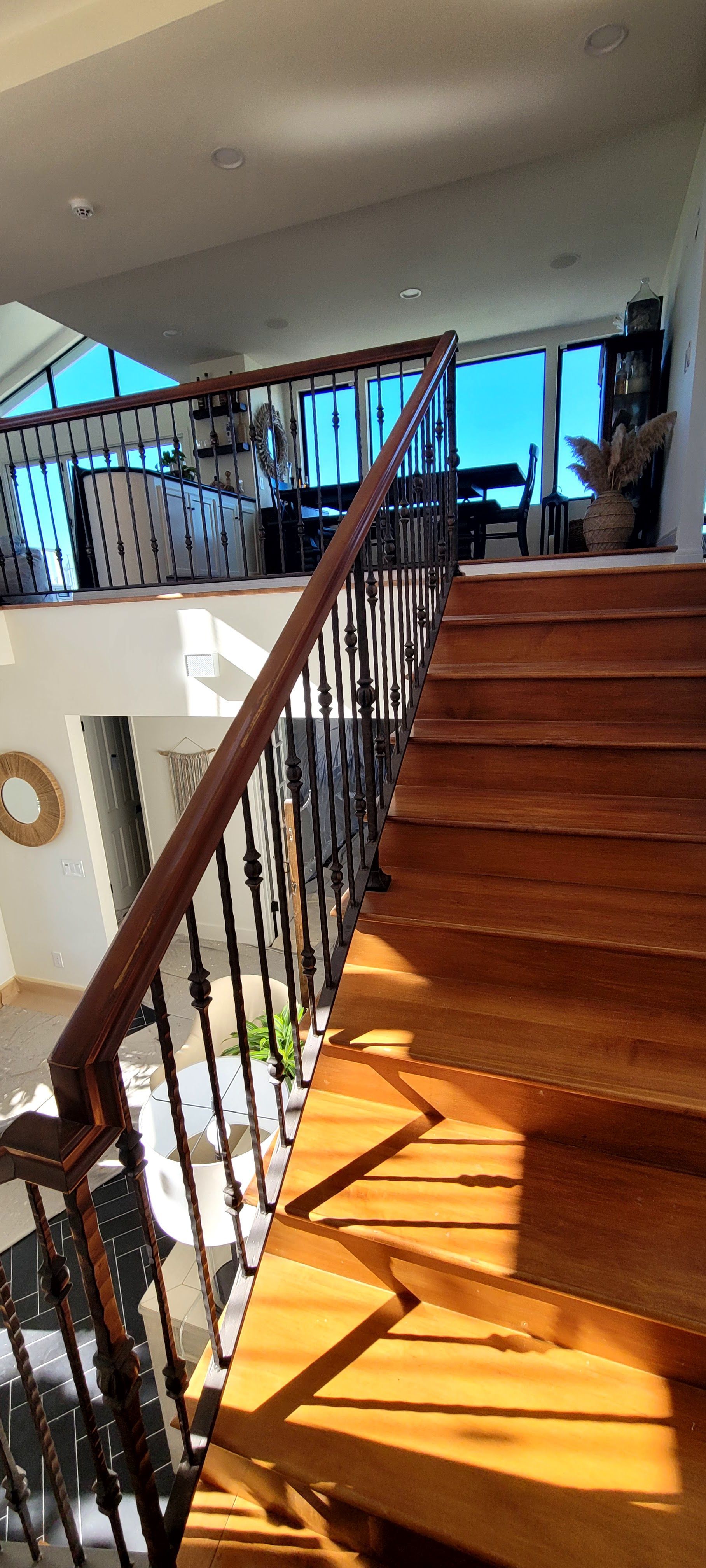 Wooden staircase with dark metal railings leading to a bright, sunlit upper landing area.