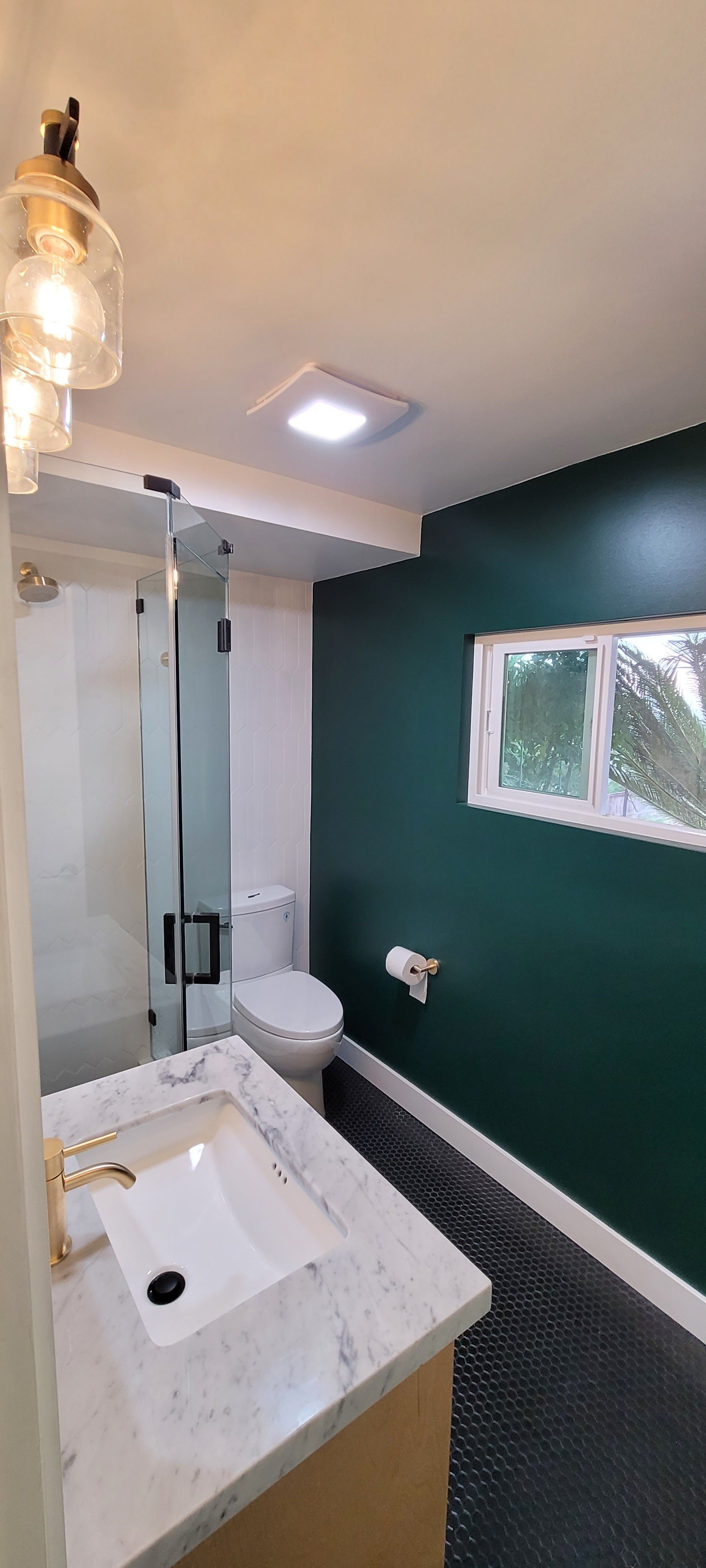 Modern bathroom with a marble vanity, glass shower, toilet, and deep green accent wall.